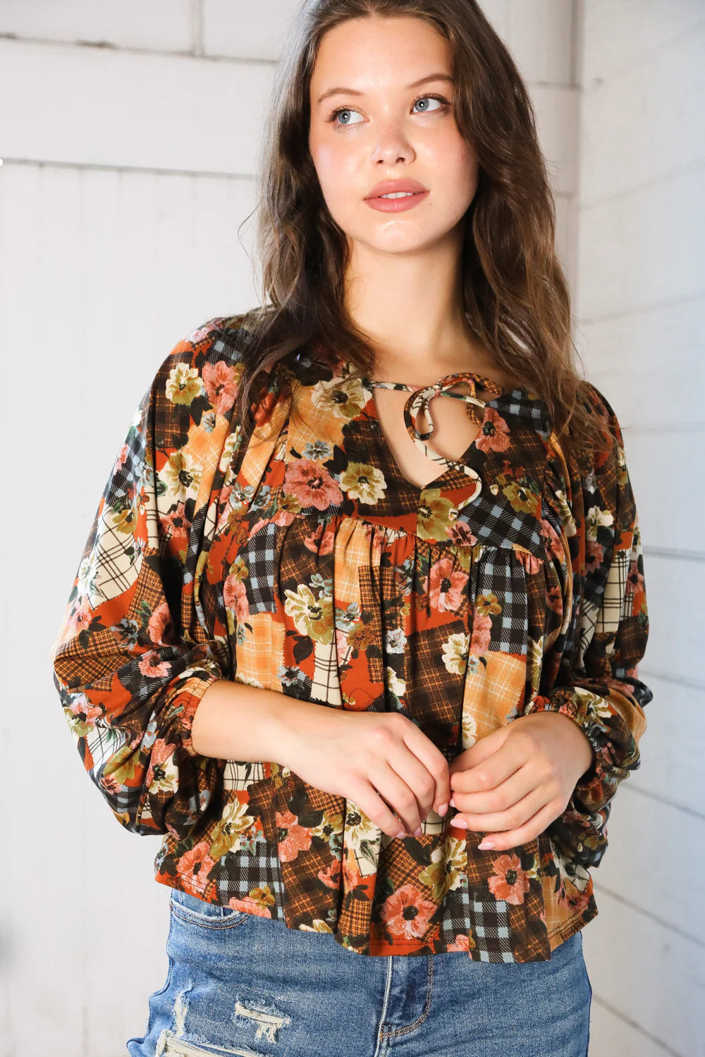 Woman wearing a floral patchwork print blouse against a white wall.