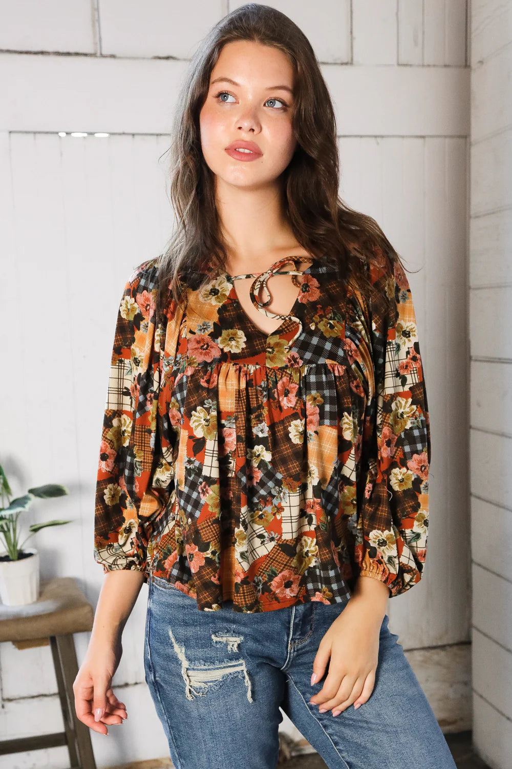 Woman wearing a floral patchwork print blouse with blue jeans indoors.