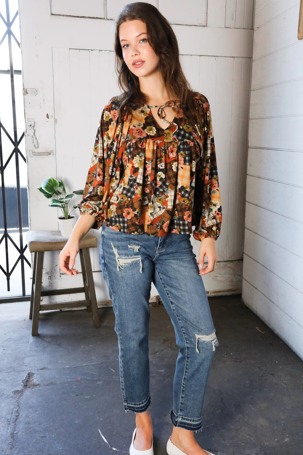Woman wearing a floral patchwork print blouse and jeans standing indoors.