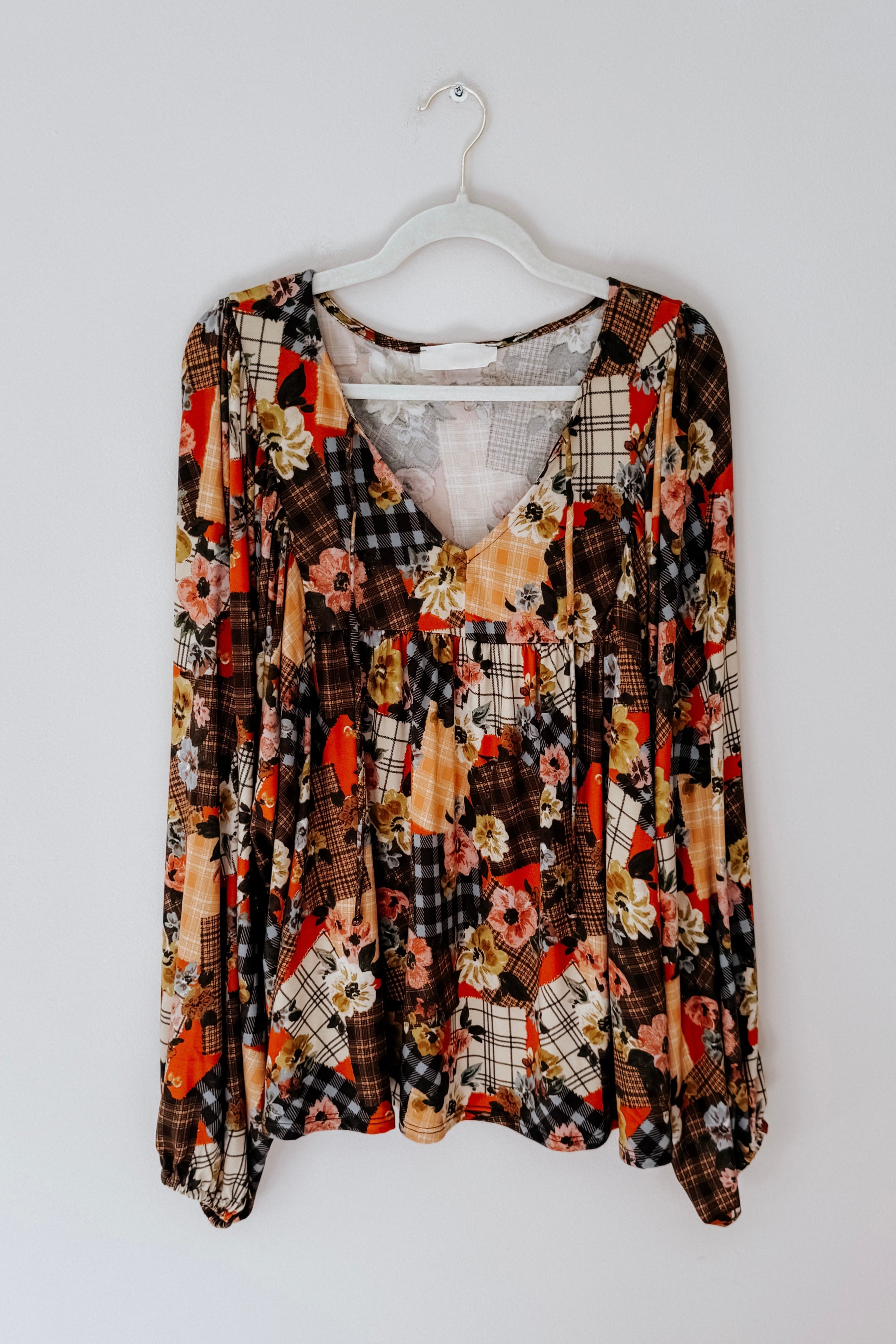 Patchwork floral print blouse on a hanger against a white background
