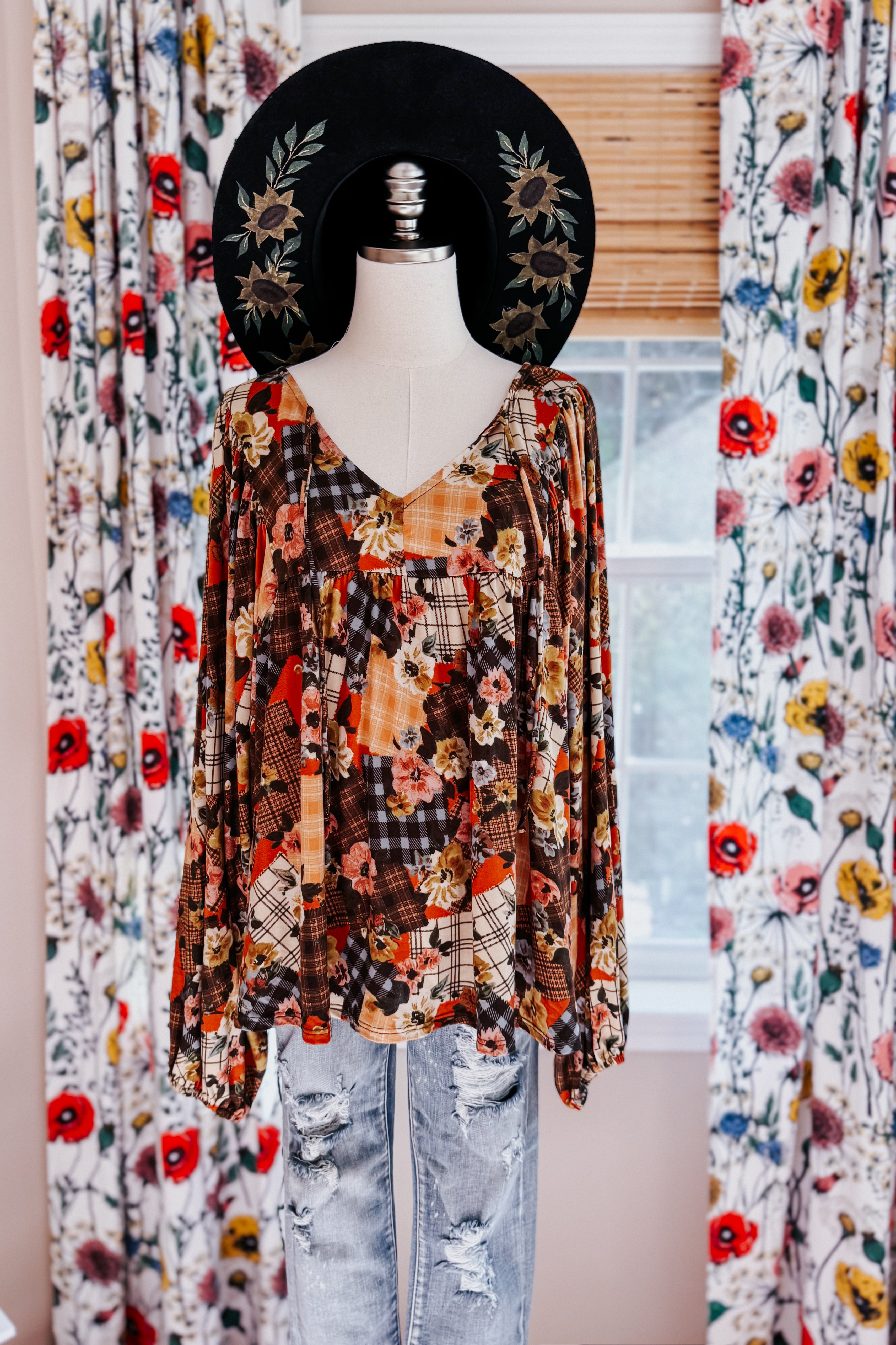 Mannequin wearing a patchwork floral print blouse and black hat with curtains in the background
