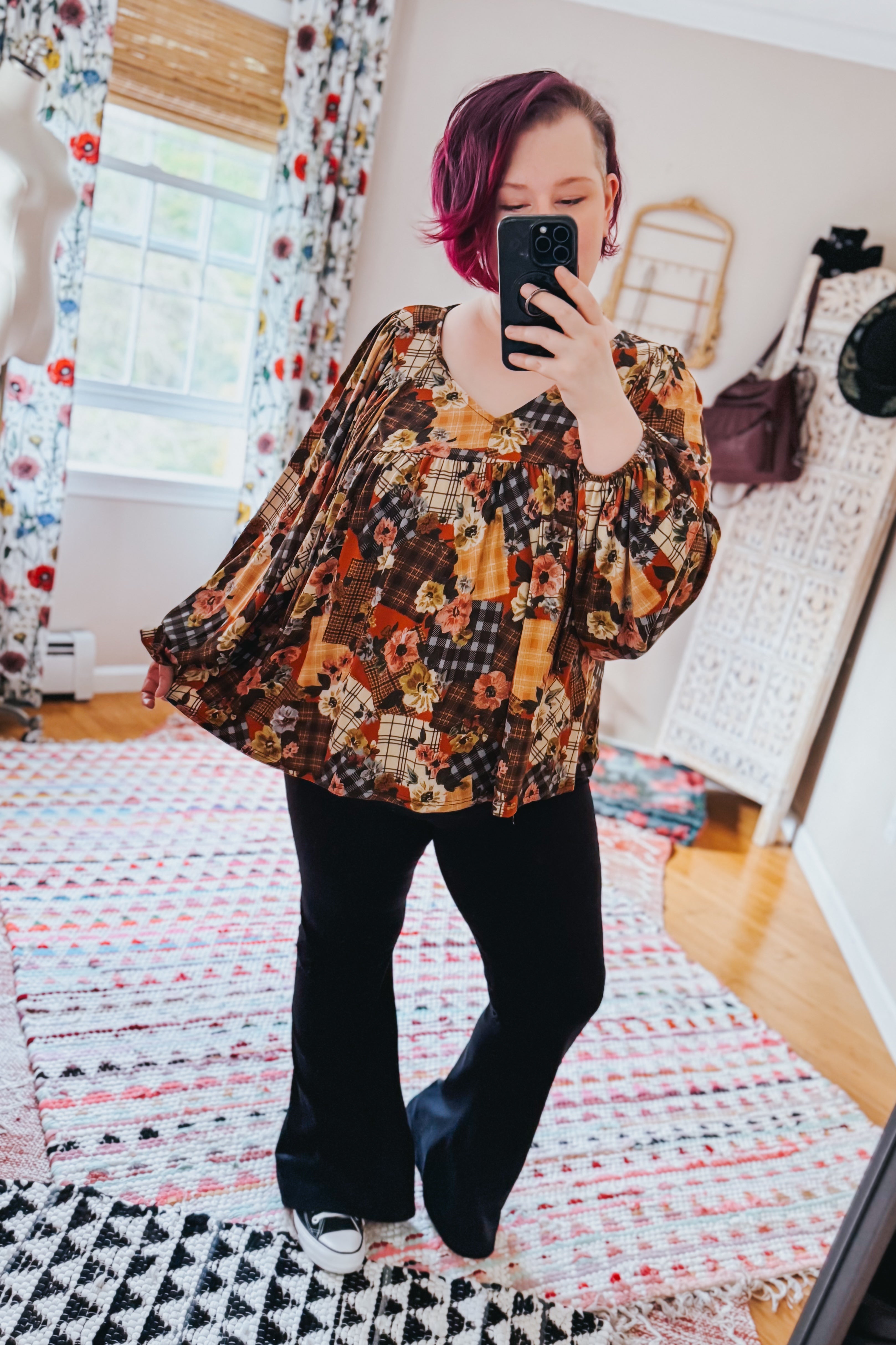 Woman wearing a floral patchwork print blouse in a room with colorful curtains and a patterned rug.