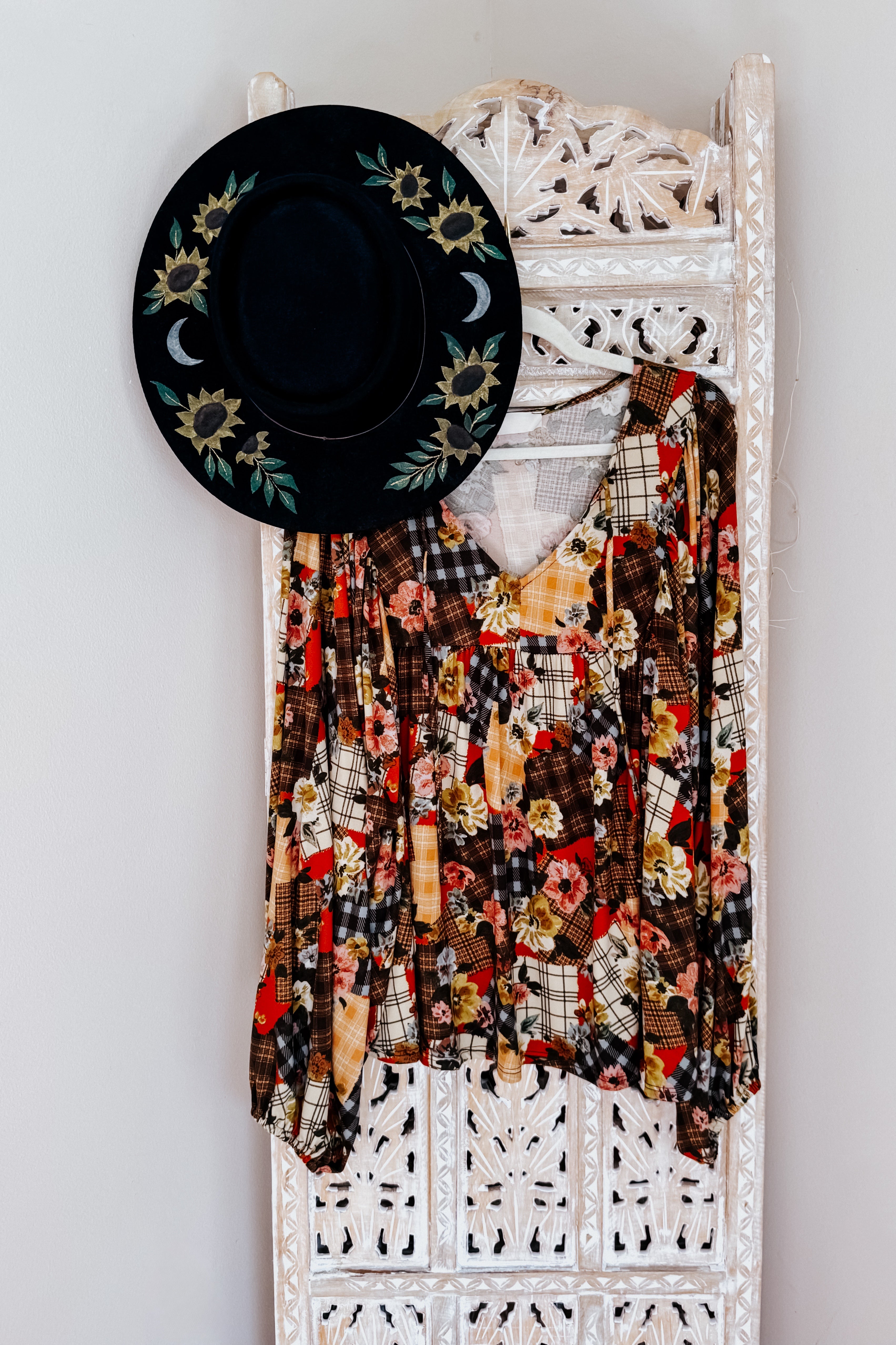 Floral patchwork print blouse hanging on a decorative white wooden rack against a light gray wall.