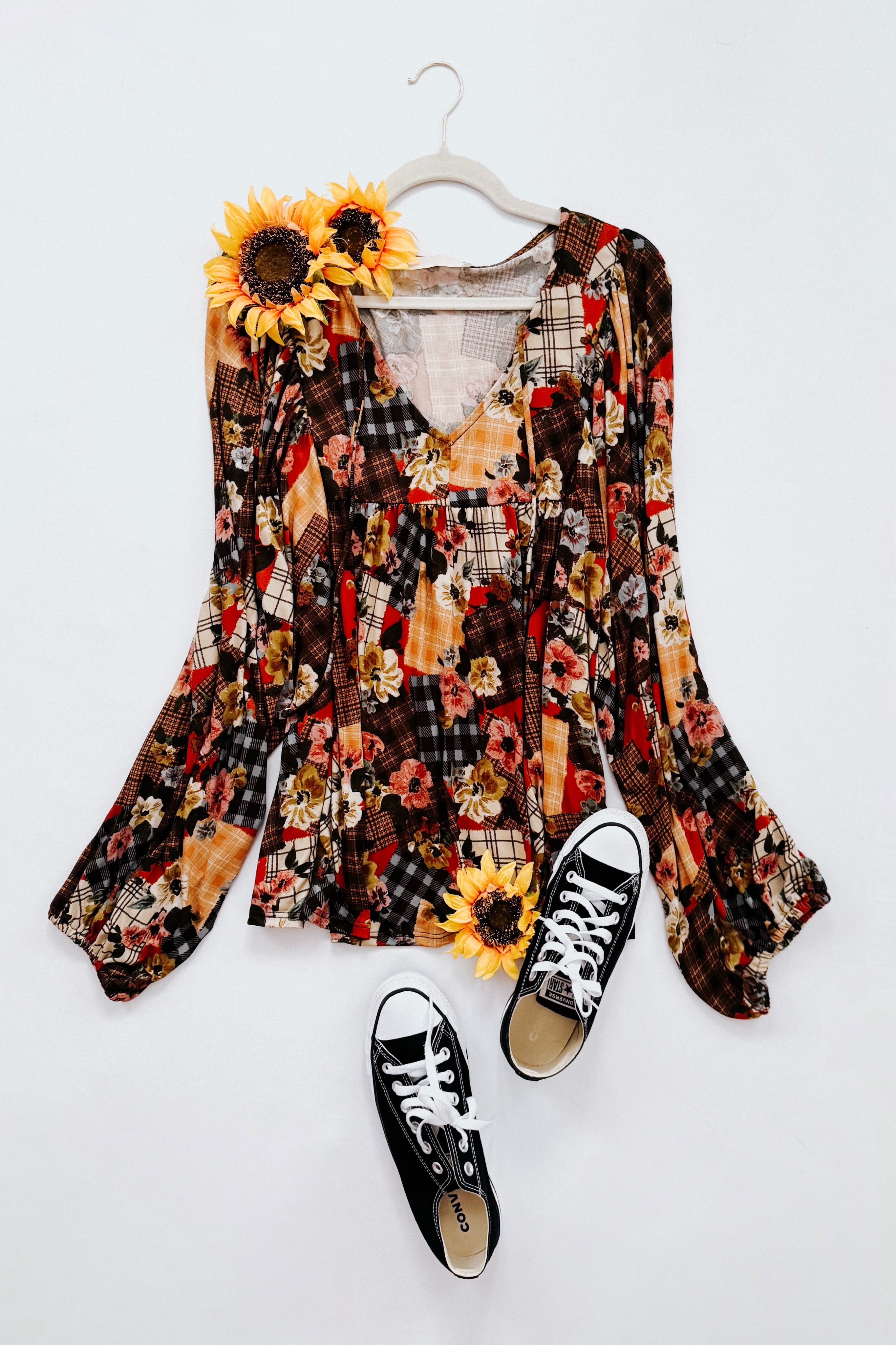 Colorful floral patchwork print blouse on a hanger with black and white sneakers on a white background