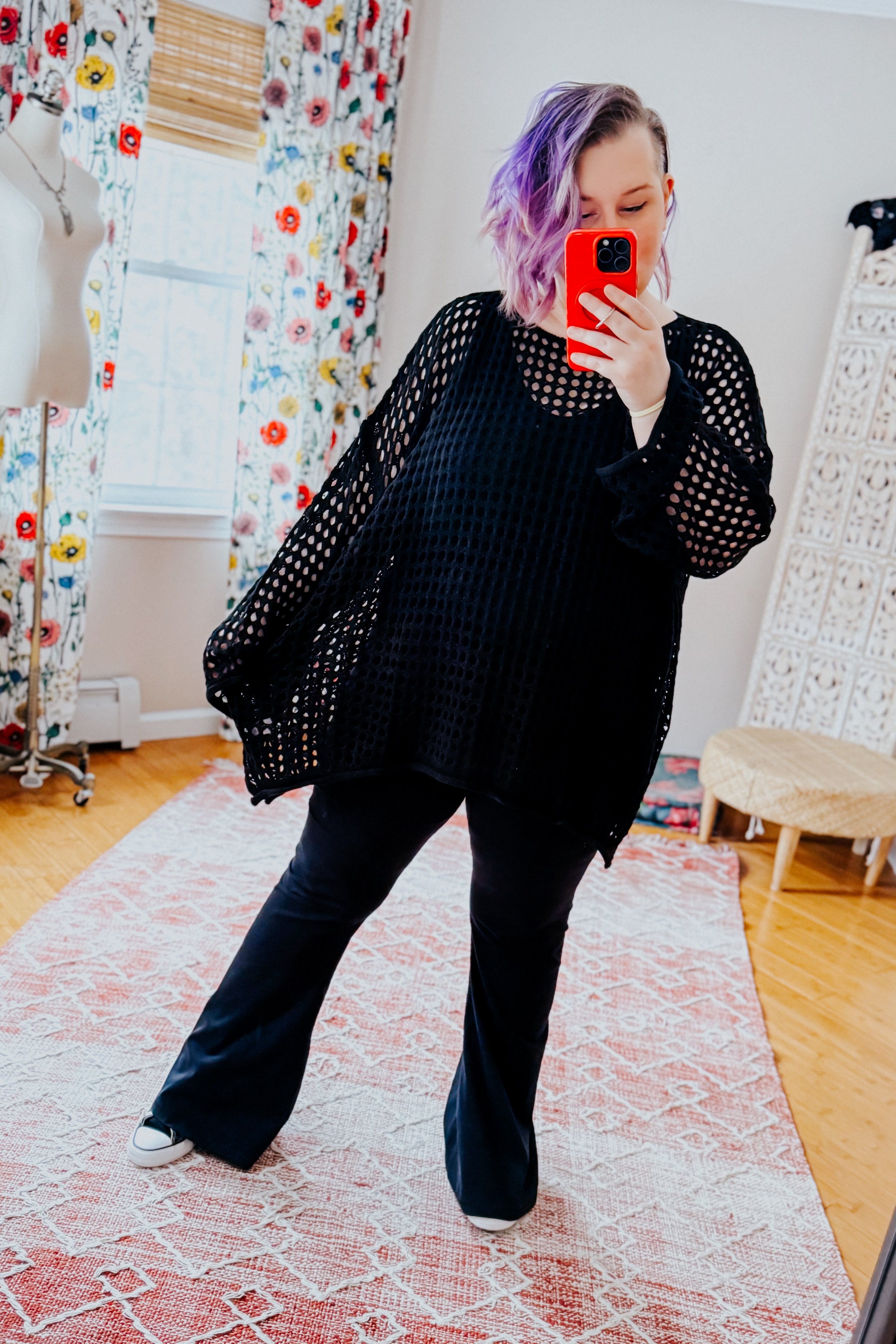 Woman with purple hair wearing oversized Ask Anyway black fishnet sweater taking mirror selfie indoors on patterned rug