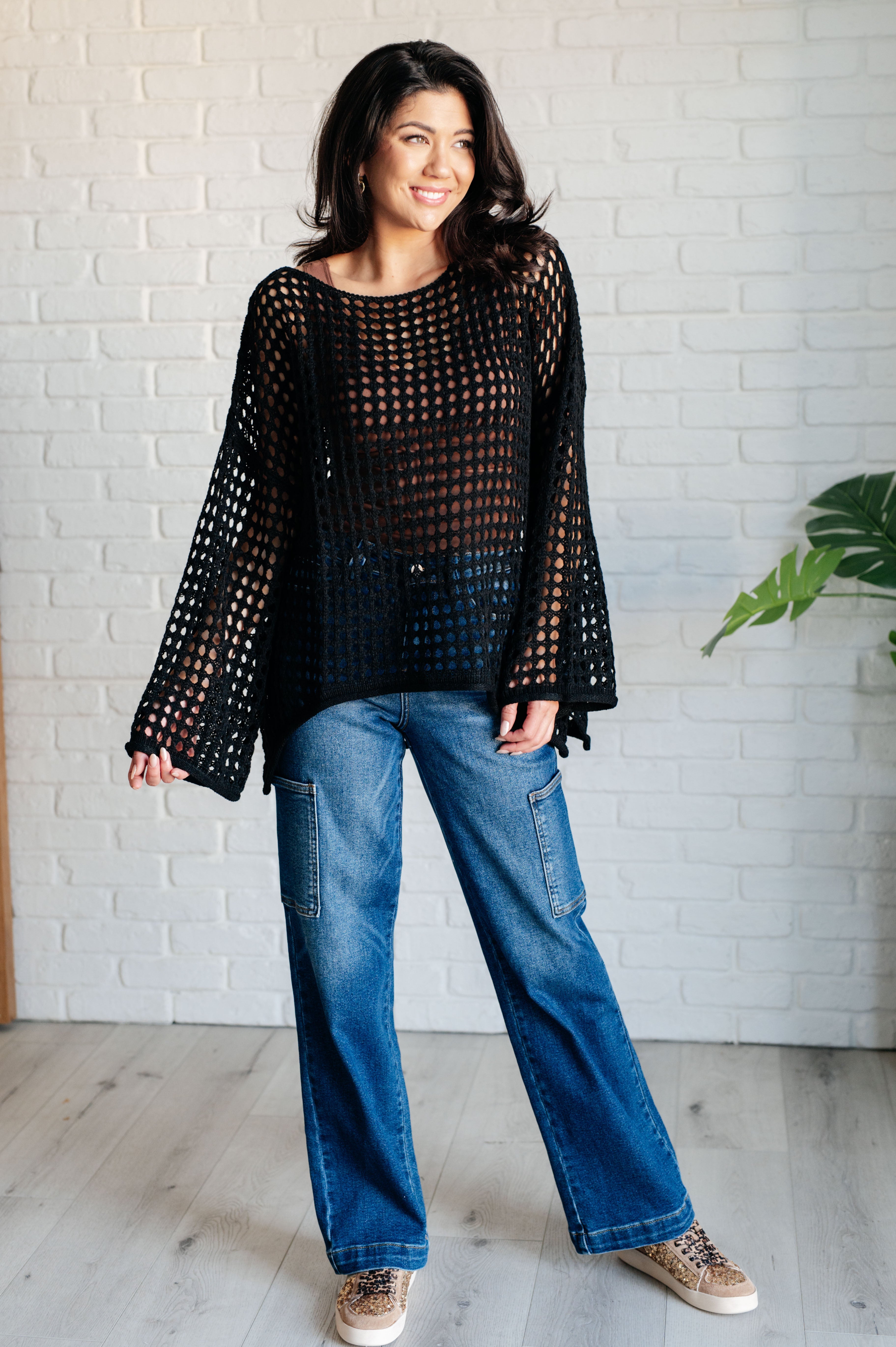 Woman wearing Ask Anyway black loose-knit fishnet sweater with wide sleeves paired with relaxed cargo jeans indoors