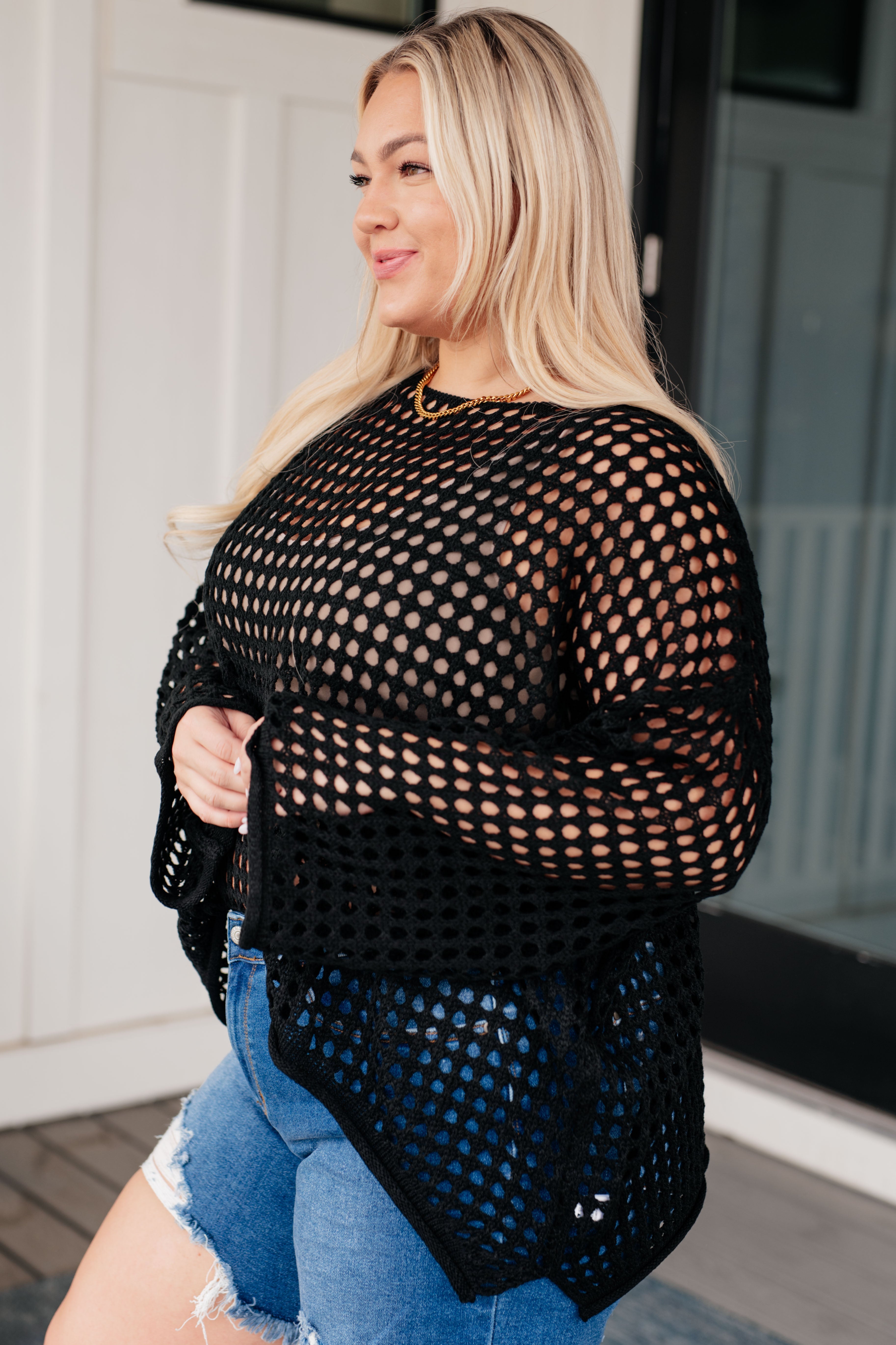 Curvy woman wearing Ask Anyway black fishnet sweater styled with distressed denim shorts outdoors by porch door