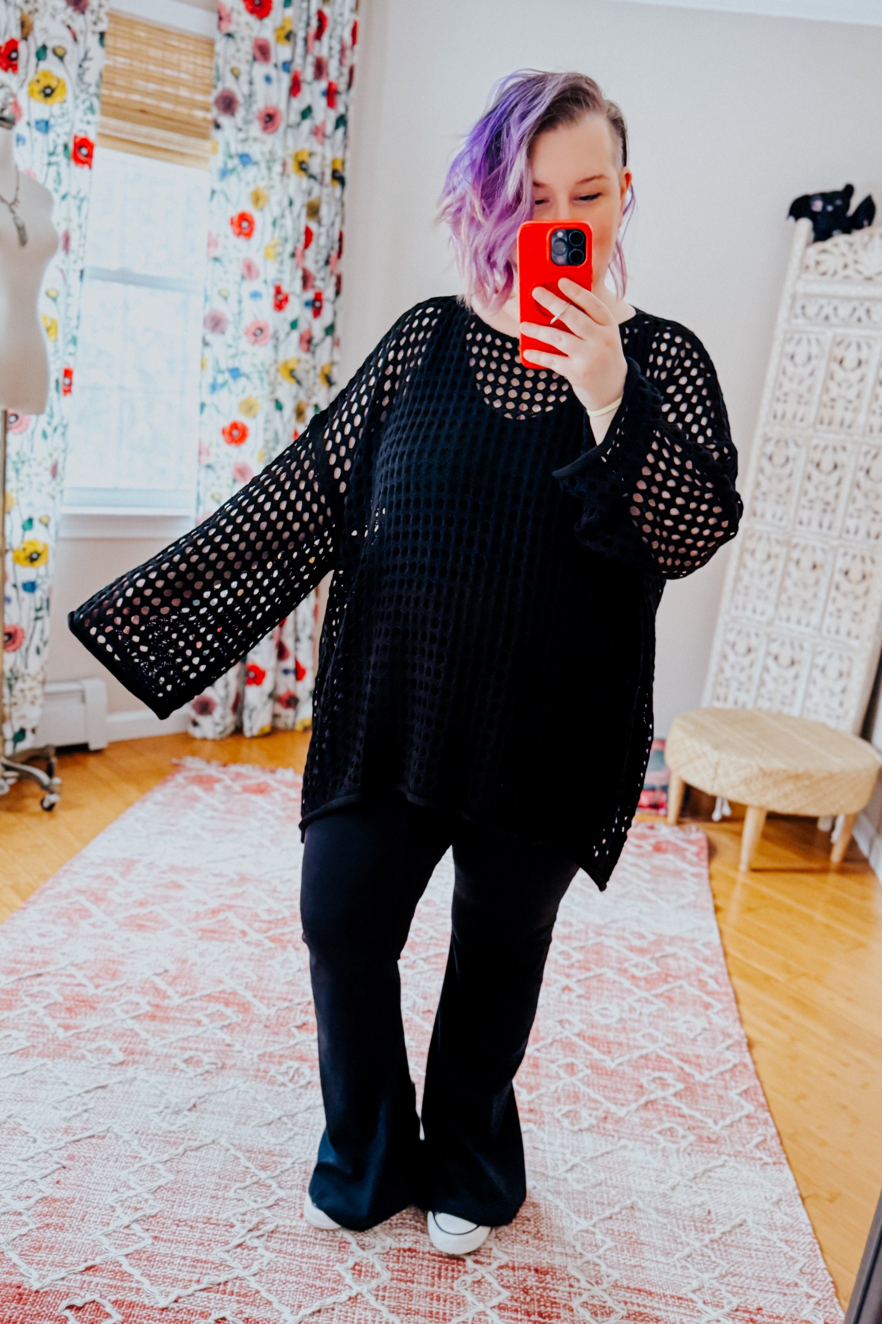 Woman with purple hair wearing Ask Anyway black oversized fishnet sweater with wide sleeves taking mirror selfie indoors
