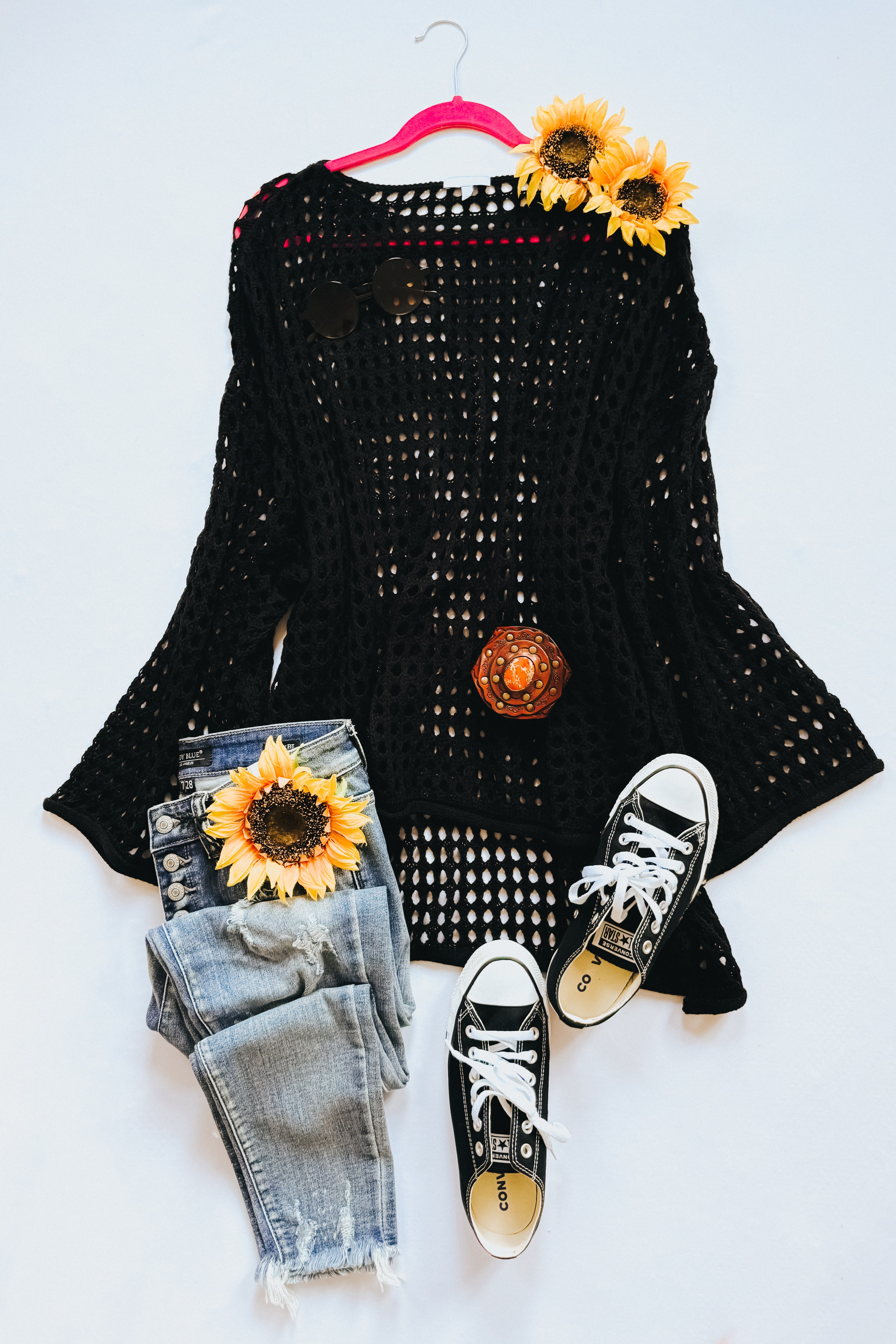 Black Ask Anyway fishnet sweater styled flat with distressed jeans, black sneakers, and sunflowers on white background