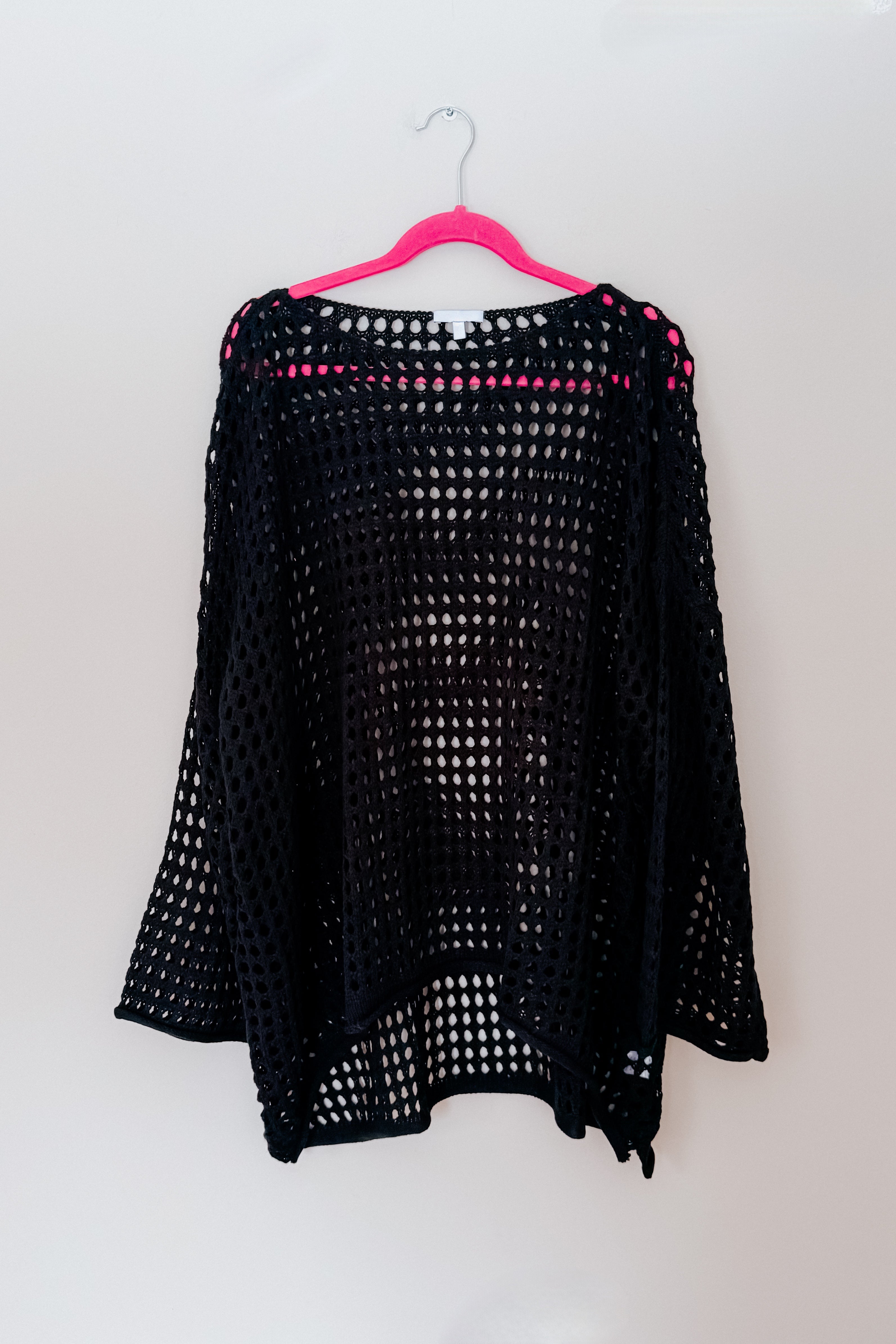 Black Ask Anyway fishnet sweater with wide sleeves hanging on bright pink hanger against plain white wall
