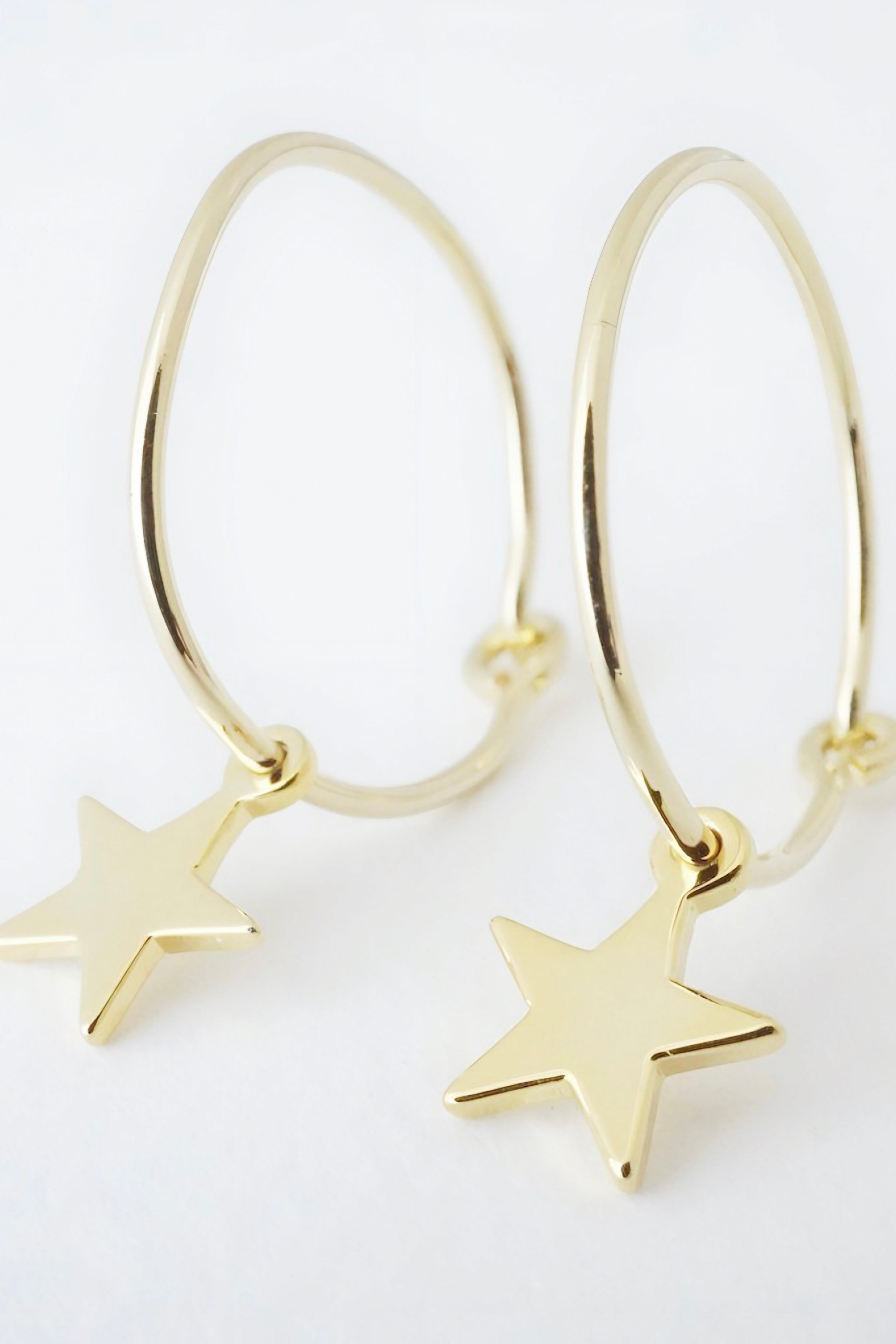 Pair of polished gold hoop earrings with smooth star charms against a soft white background AstraMagicCharmStarHoopEarrings10.jpg
