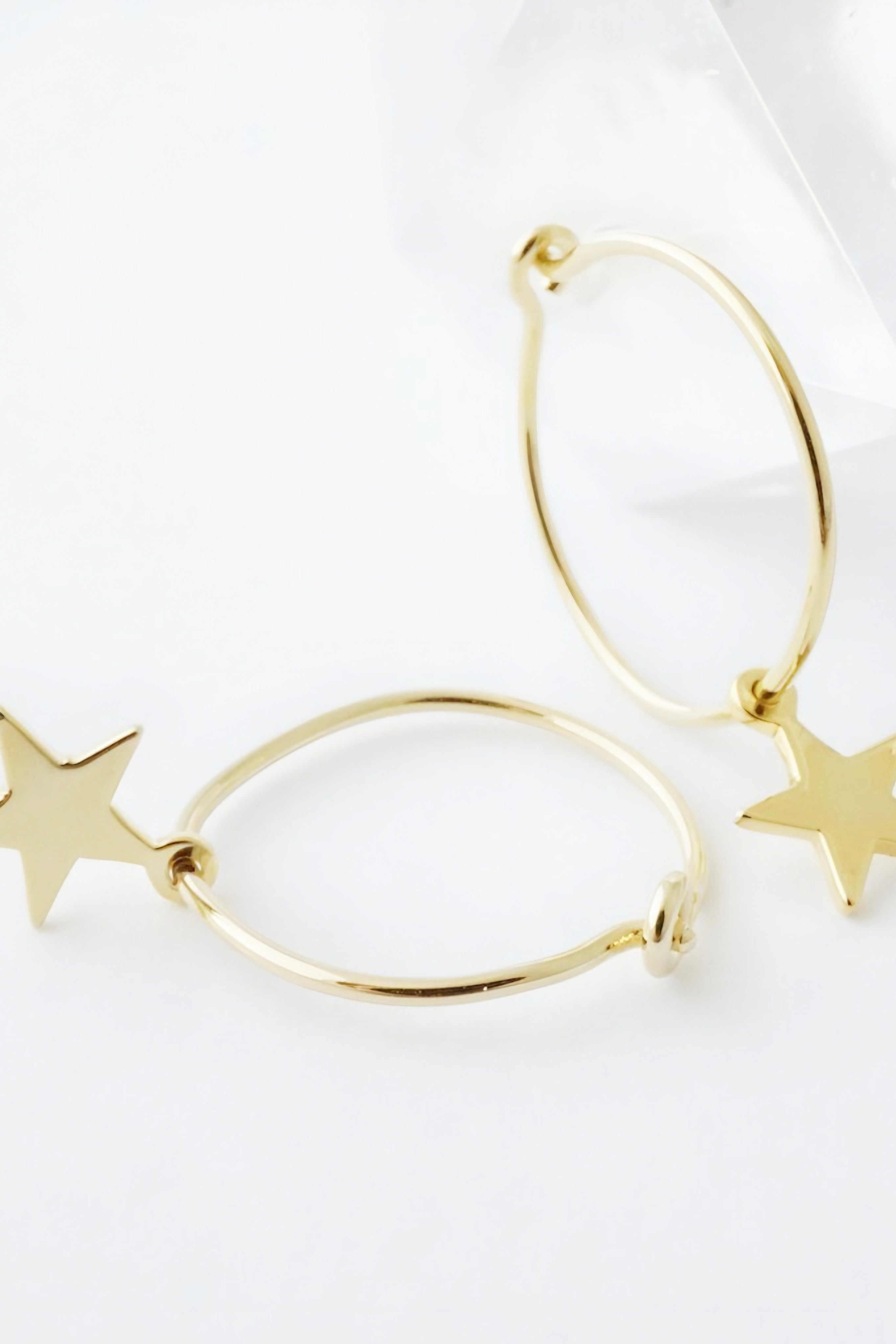 Close-up of thin gold hoop earrings with flat star charms on a white background AstraMagicCharmStarHoopEarrings8.jpg