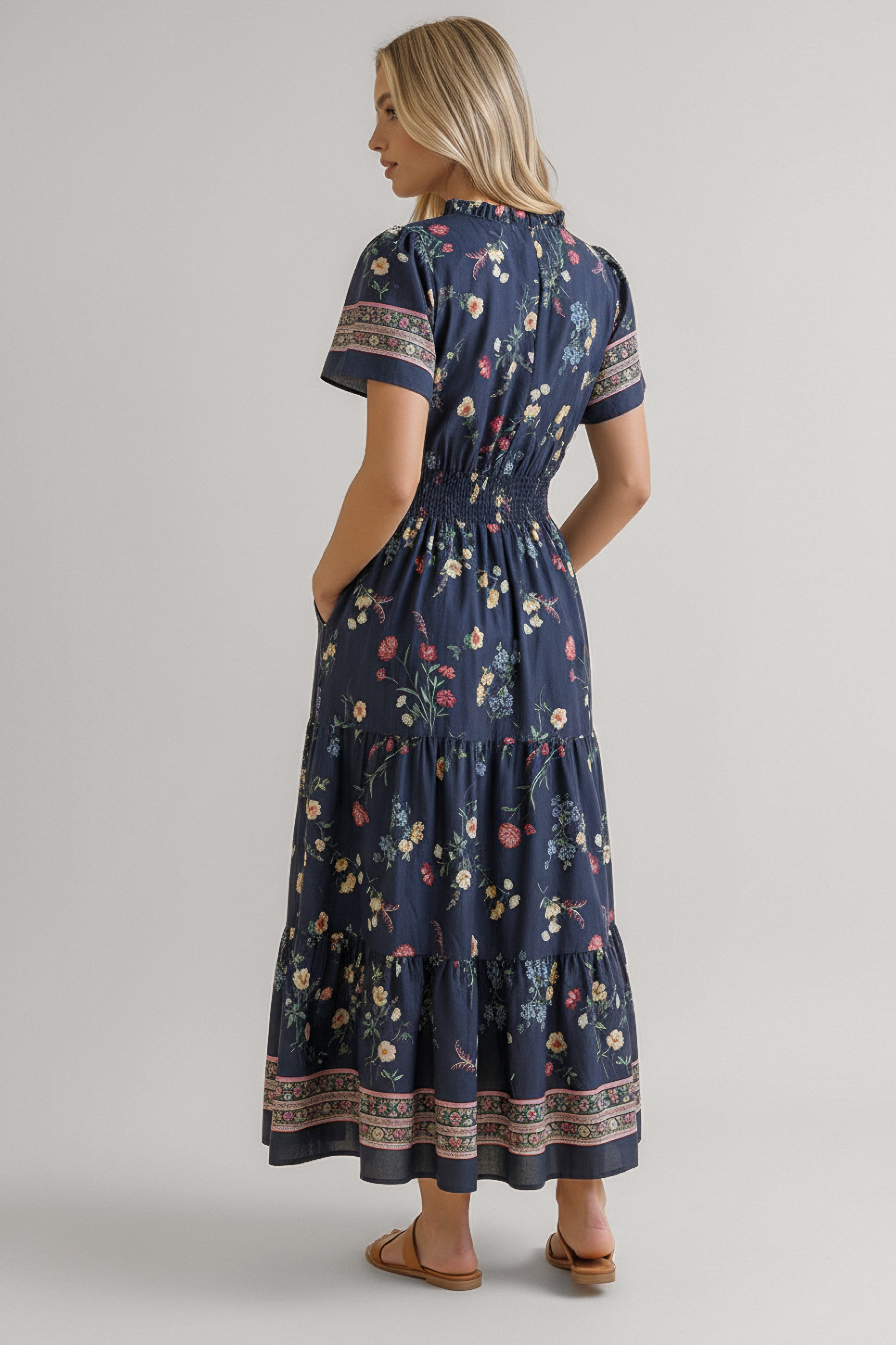 Woman in a navy floral maxi dress with short sleeves, smocked waist, and patterned hems standing with hands in pockets