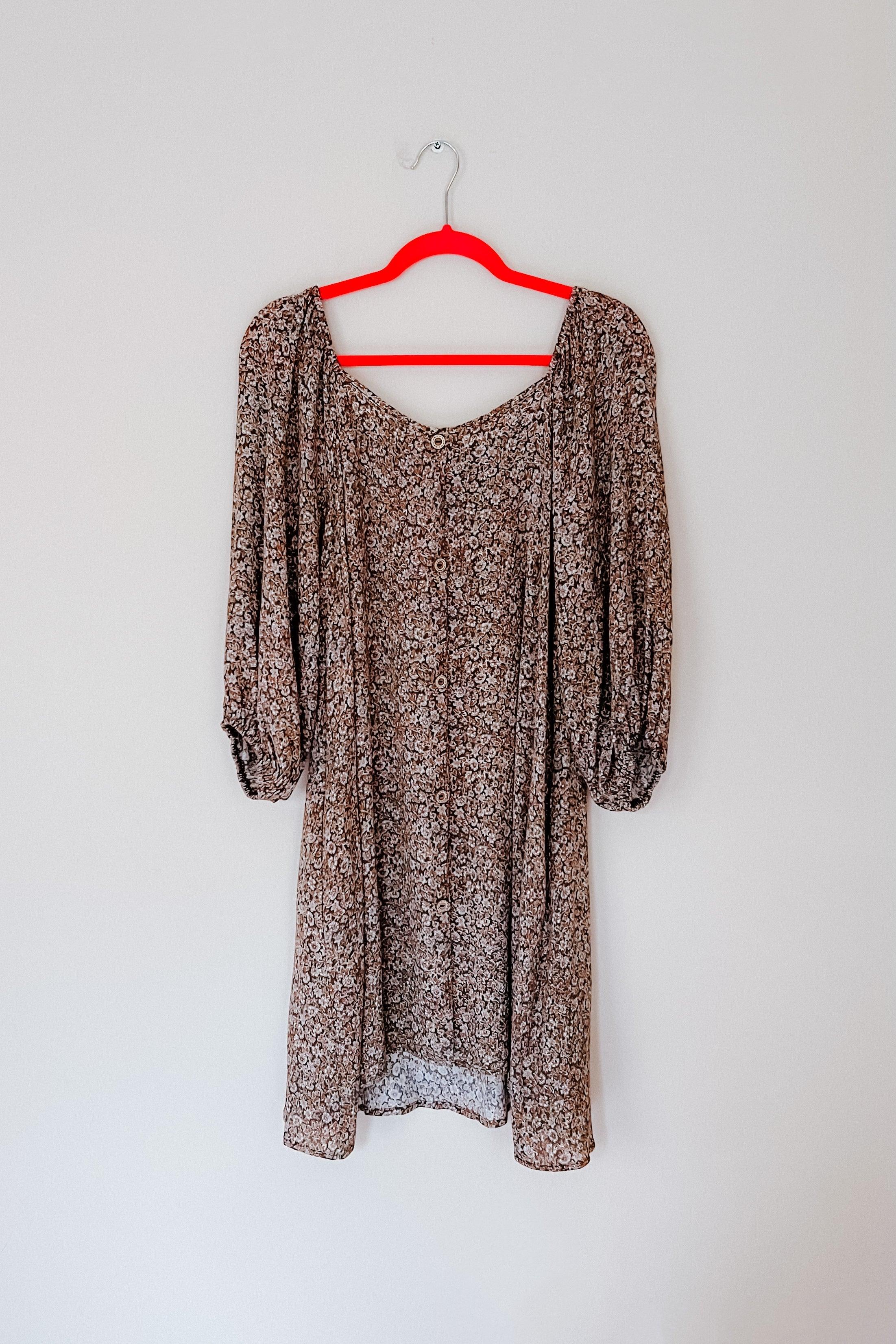 Autumn Feels Floral Dress hanging on red hanger showing button-down front and puff sleeve details against white wall