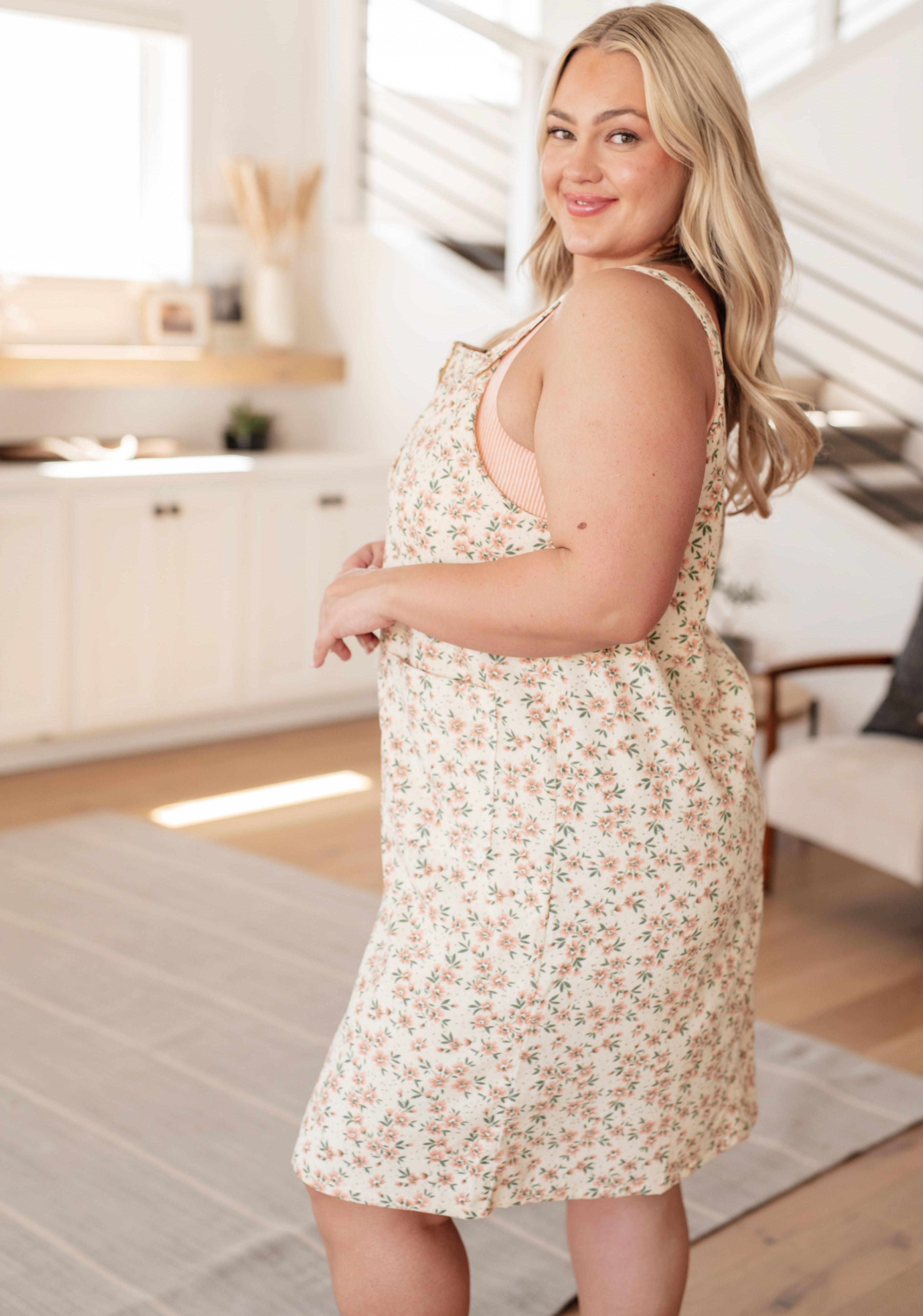 Plus size model in floral Baby Blossoms Jumper layered over striped top in bright living space, angled side view