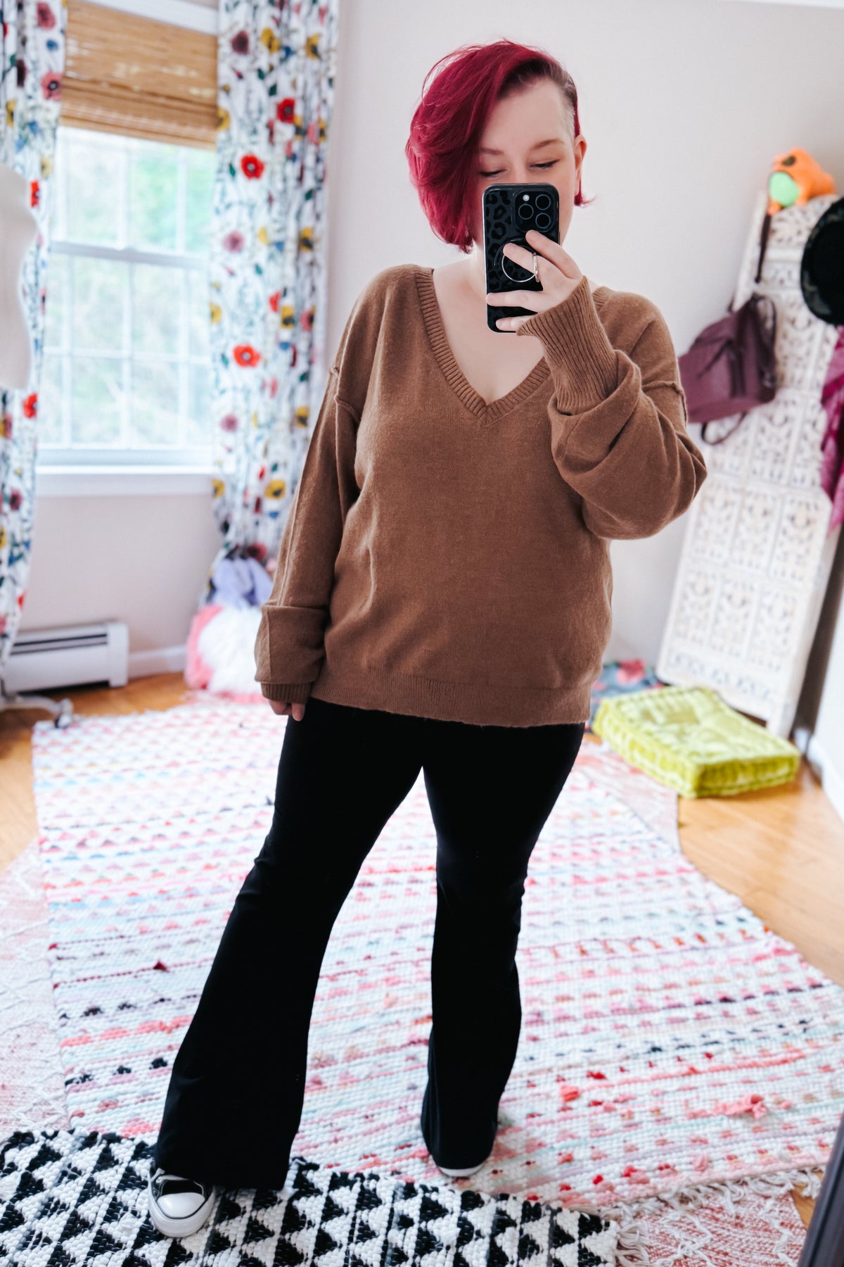 Mocha V-neck sweater with dropped shoulders and exposed seams styled with black flared pants in a casual mirror selfie