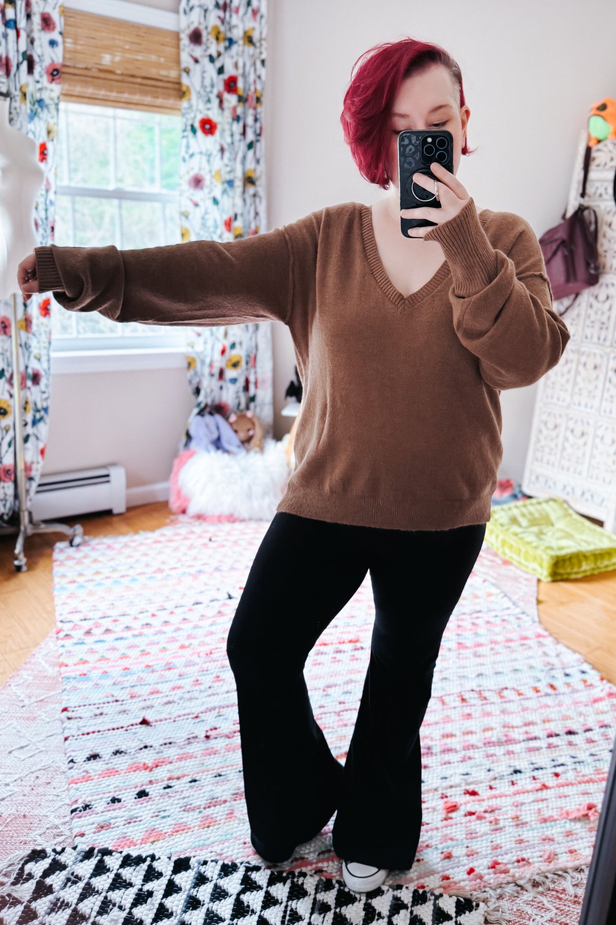Mocha V neck sweater with dropped shoulders and exposed seams styled with black flared pants in a cozy bedroom
