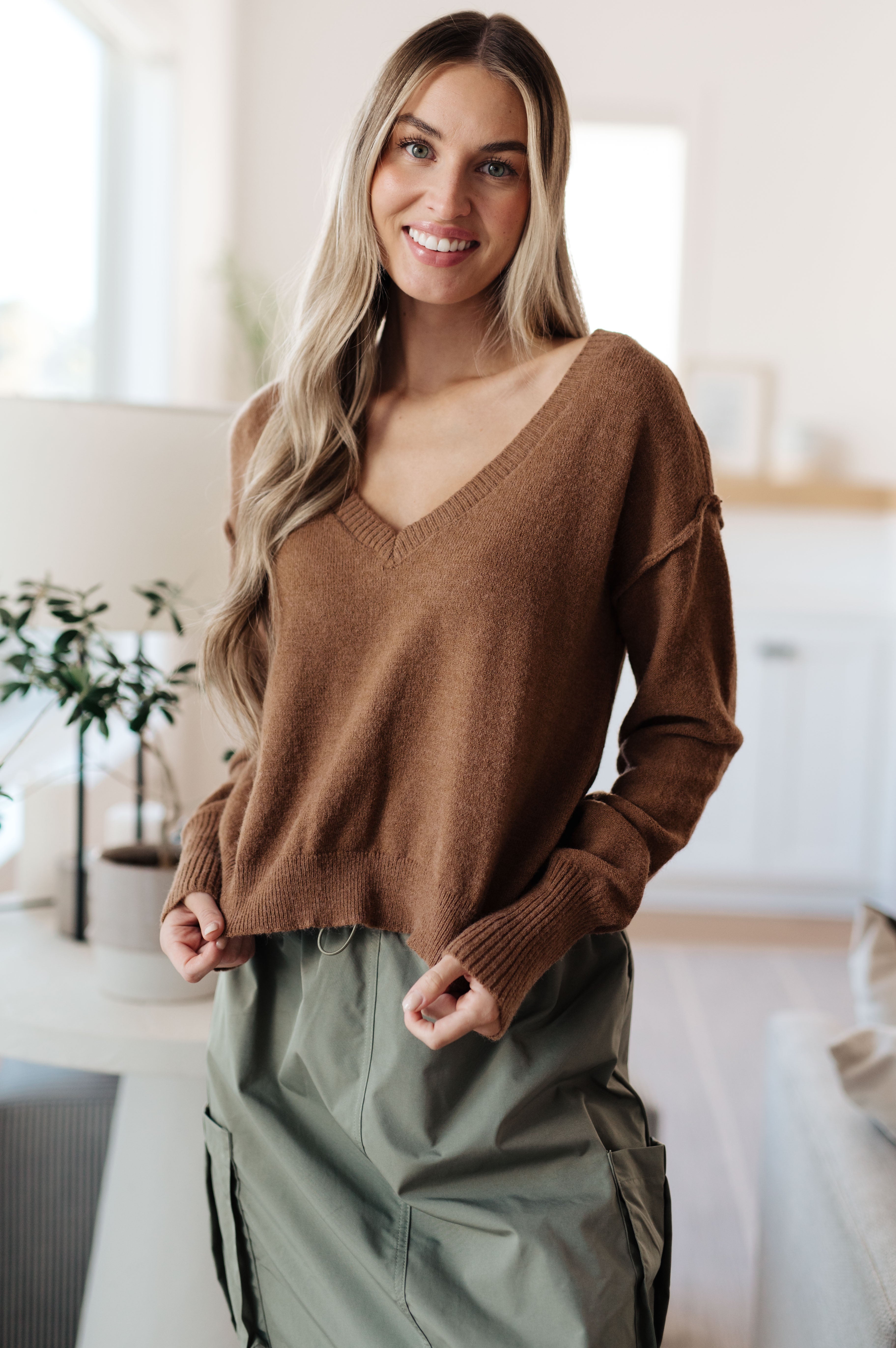 Woman smiling wearing mocha Back to Life V-Neck Sweater with dropped shoulders in bright room, front view