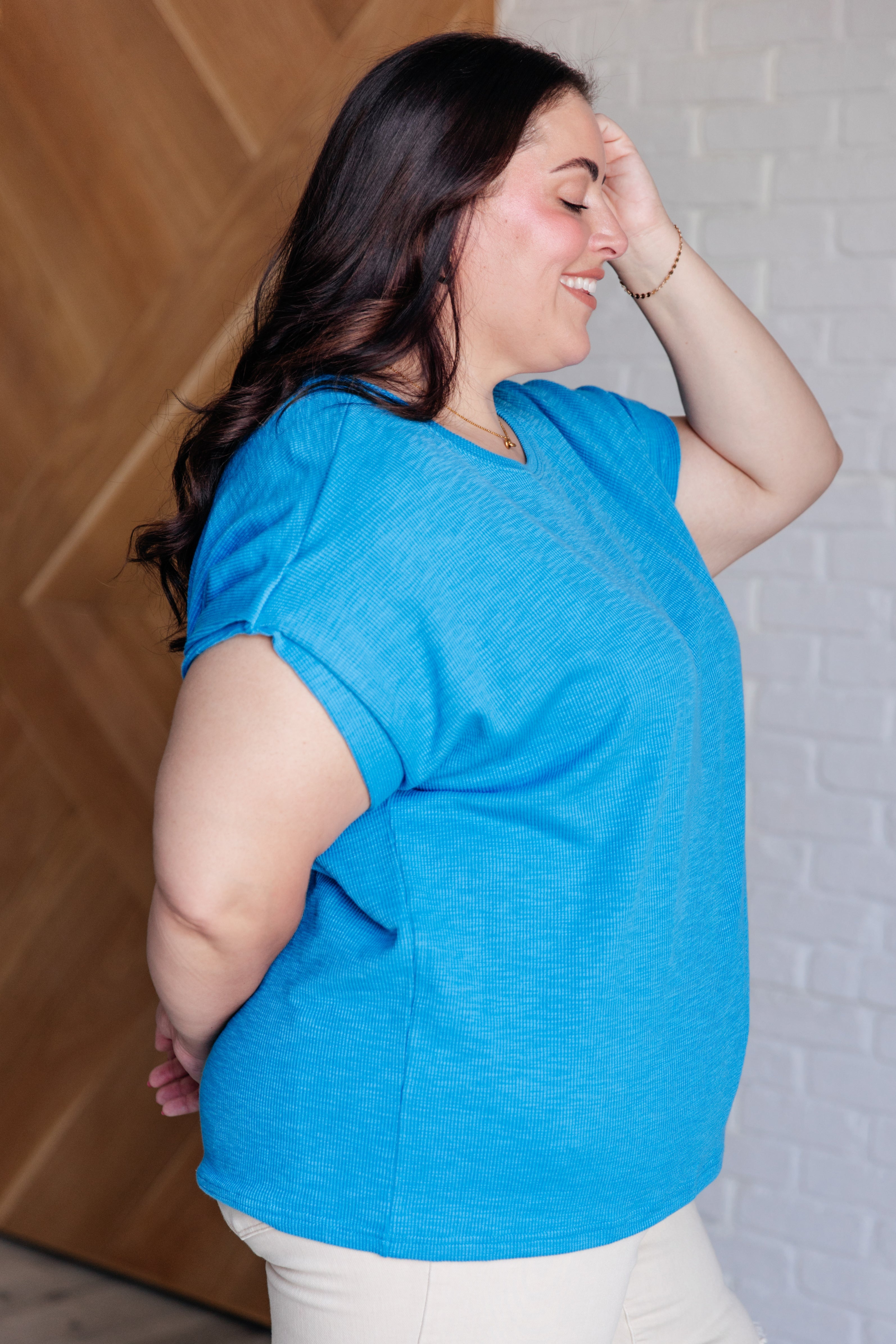 Plus size woman smiling wearing bright blue short sleeve top from Back to My Favorite Place set, side profile indoors
