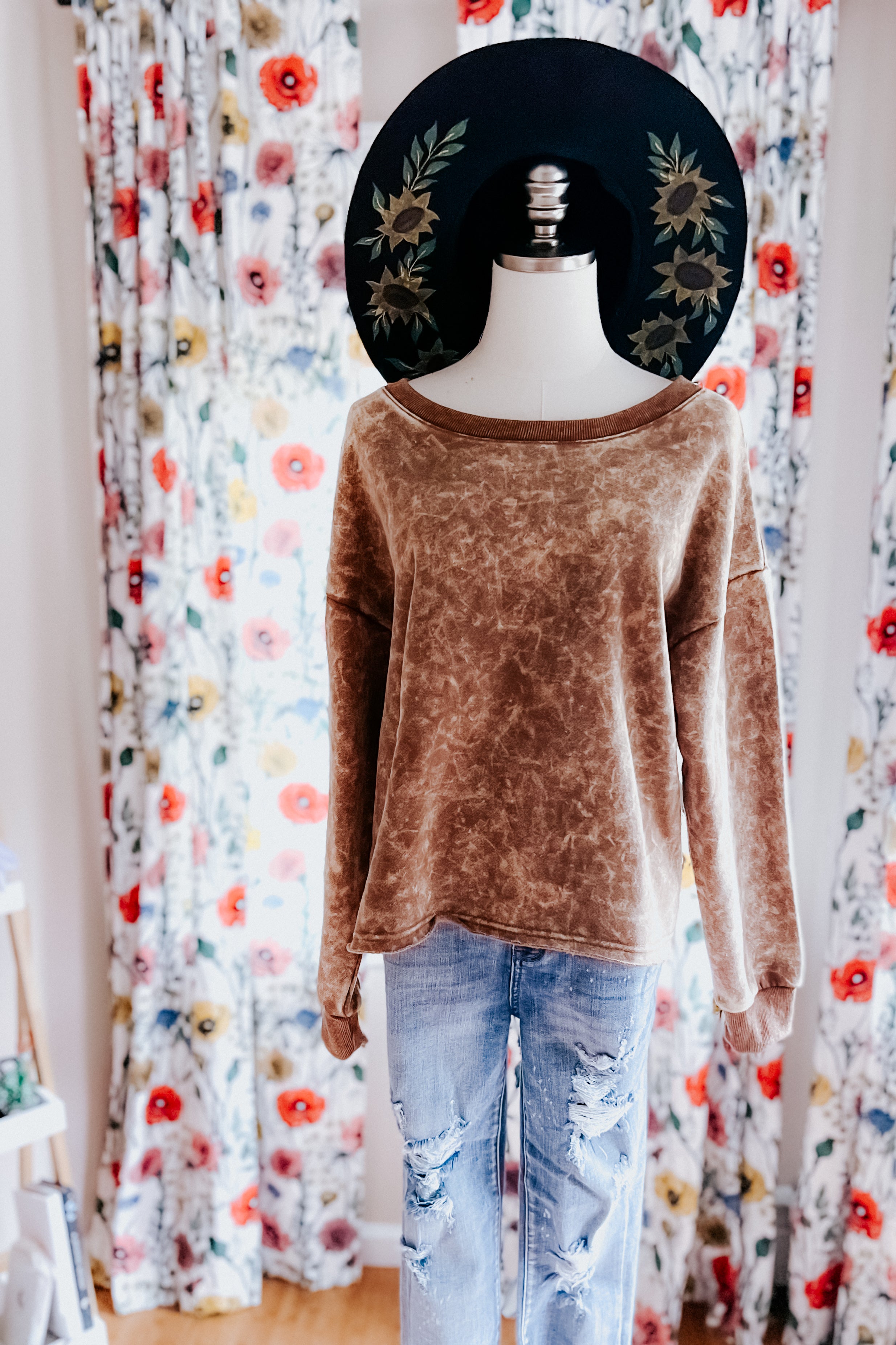 Mannequin dressed in mocha acid wash long sleeve cropped pullover paired with ripped light blue jeans and black floral hat indoors