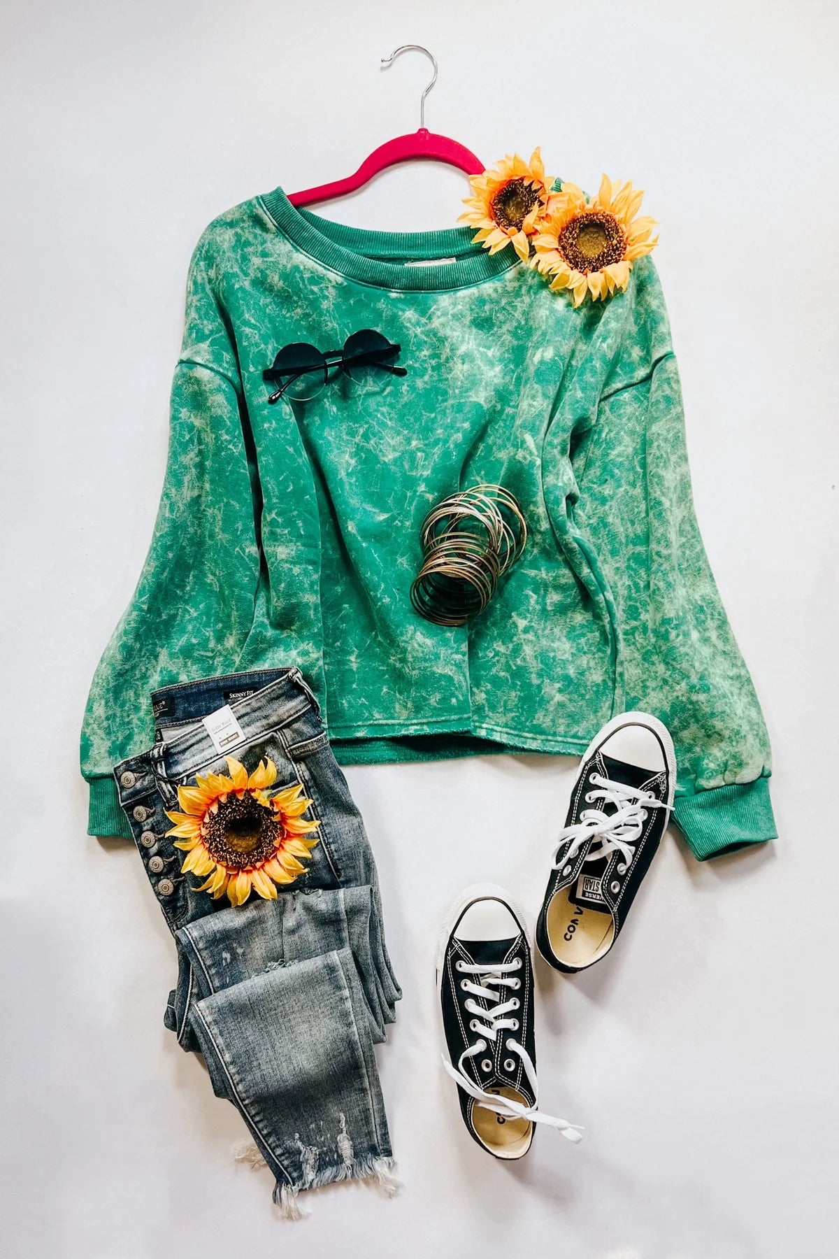 Sea green acid wash cropped pullover styled with distressed jeans, black Converse sneakers, sunglasses, bracelets, and sunflowers flat lay, IMG_9832.webp
