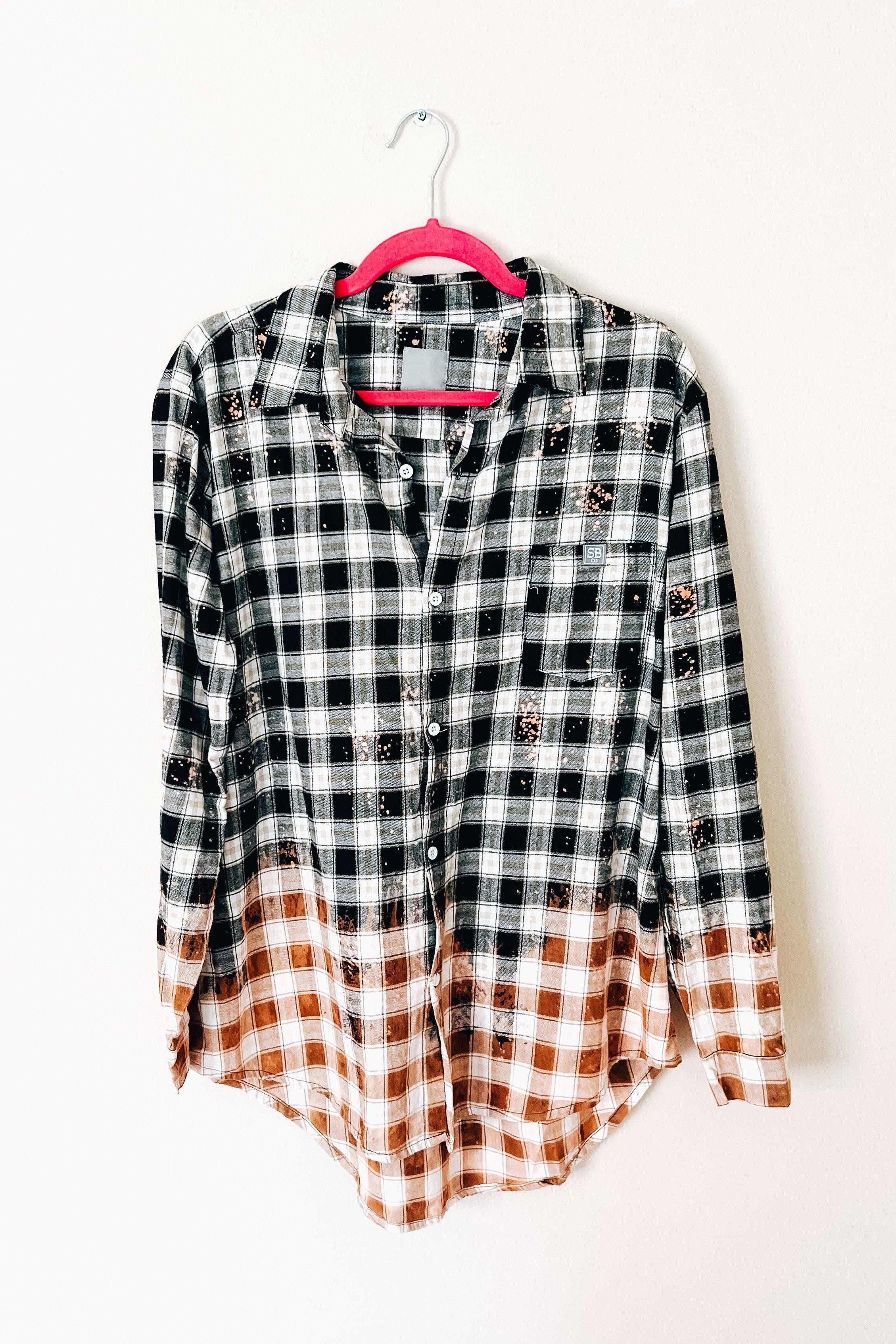 Black and brown bleached plaid flannel shirt with button front hanging on pink hanger against white background