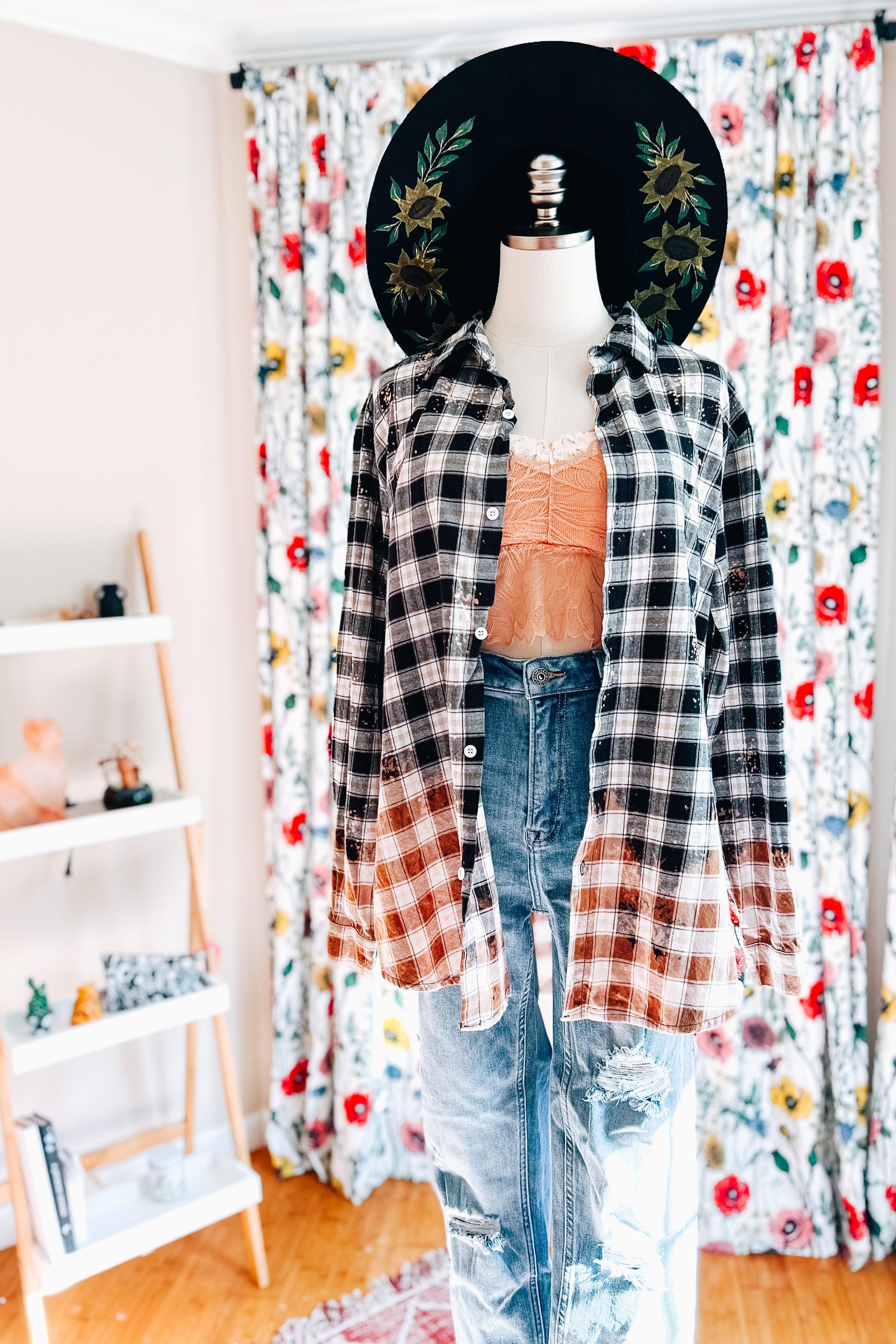 Mannequin dressed in gradient black and brown bleach-dyed plaid flannel shirt with distressed jeans and floral hat indoors