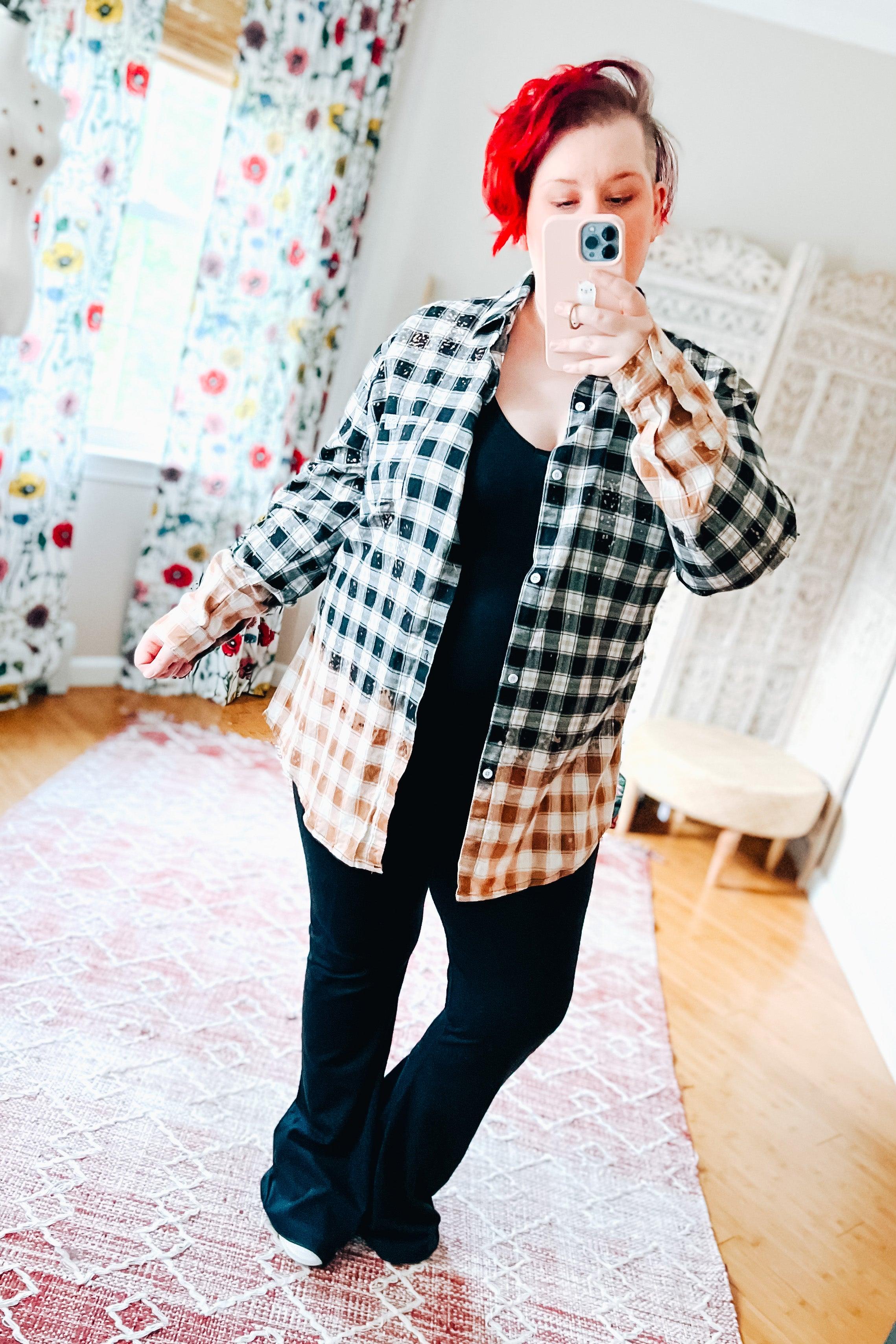 Person taking mirror selfie wearing black and brown bleached plaid flannel shirt with black outfit indoors.