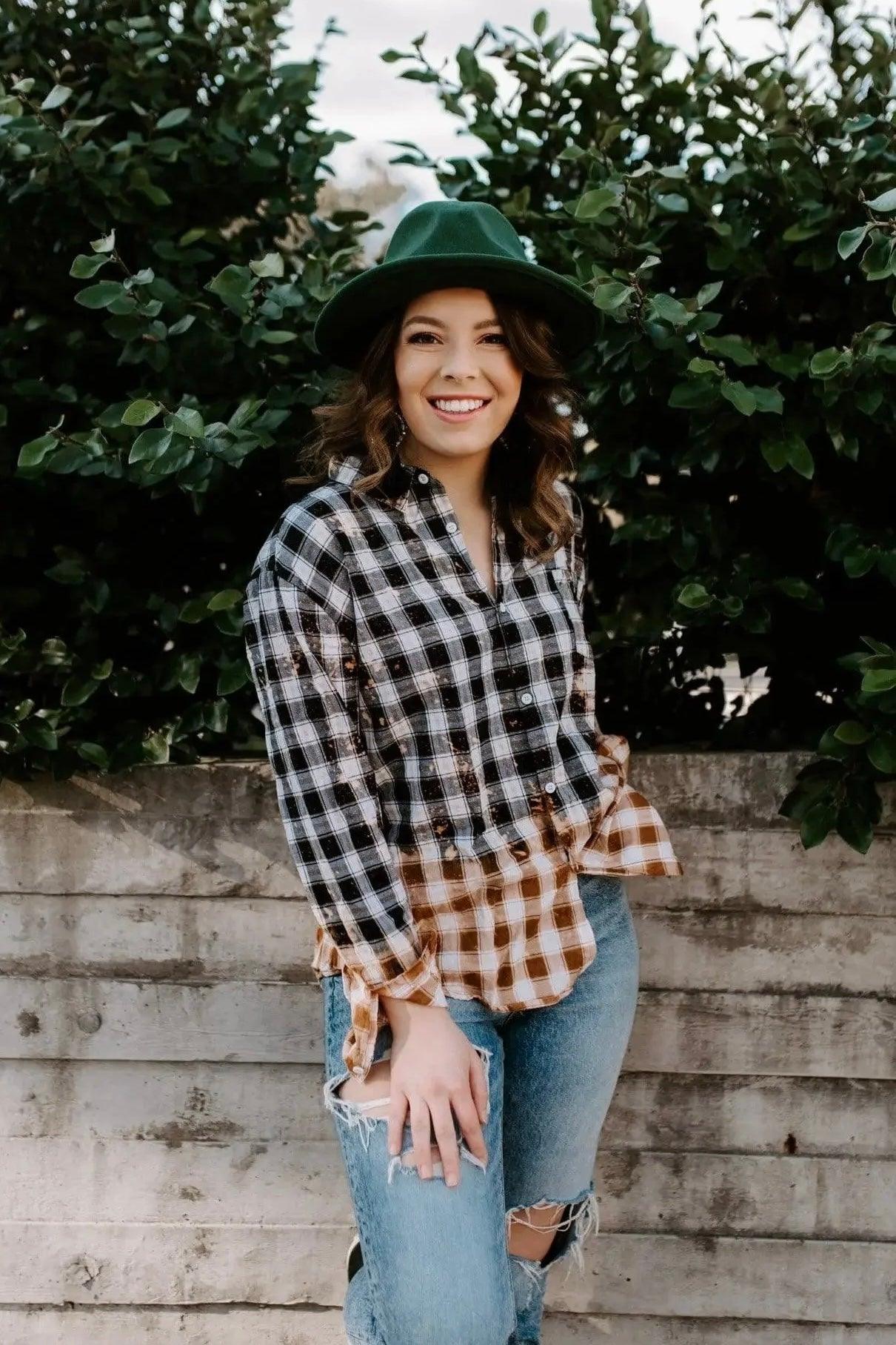Woman wearing unique black and brown bleached plaid flannel shirt with ripped jeans standing by concrete wall outdoors