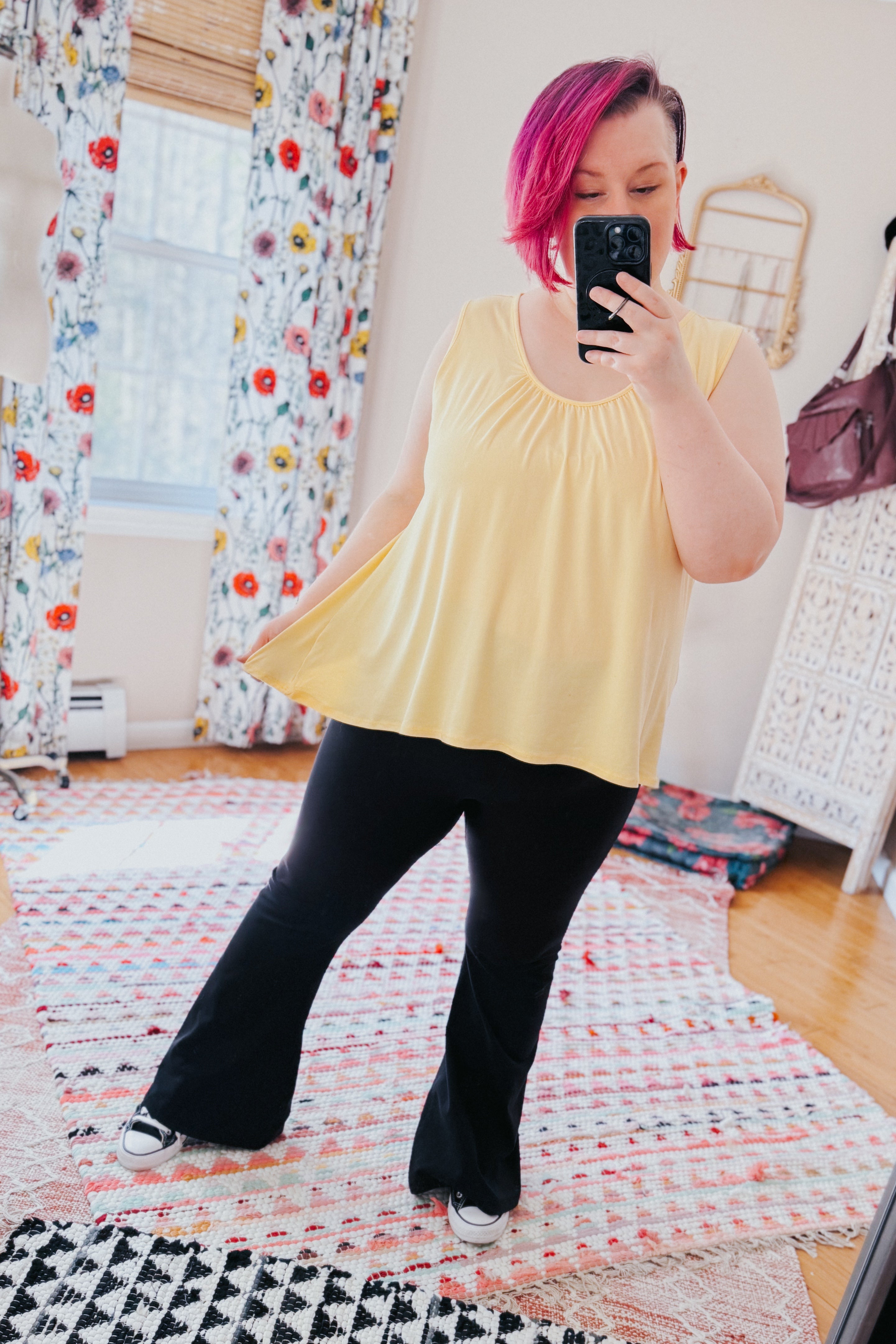 Person with pink hair taking mirror selfie wearing flowy yellow Banana Bliss tank top and black flare pants indoors