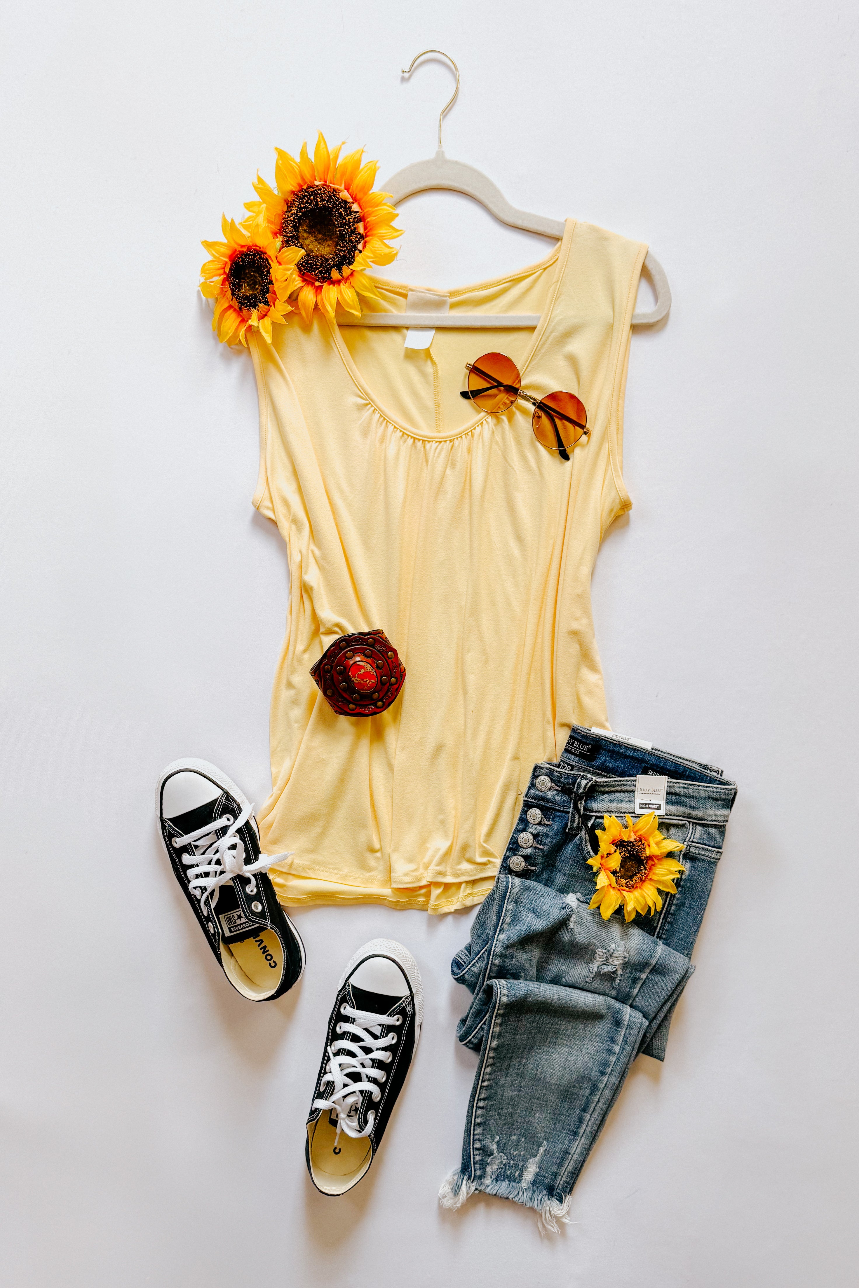 Yellow Banana Bliss tank top displayed flat with sunglasses, distressed jeans, black sneakers, and sunflowers on white background