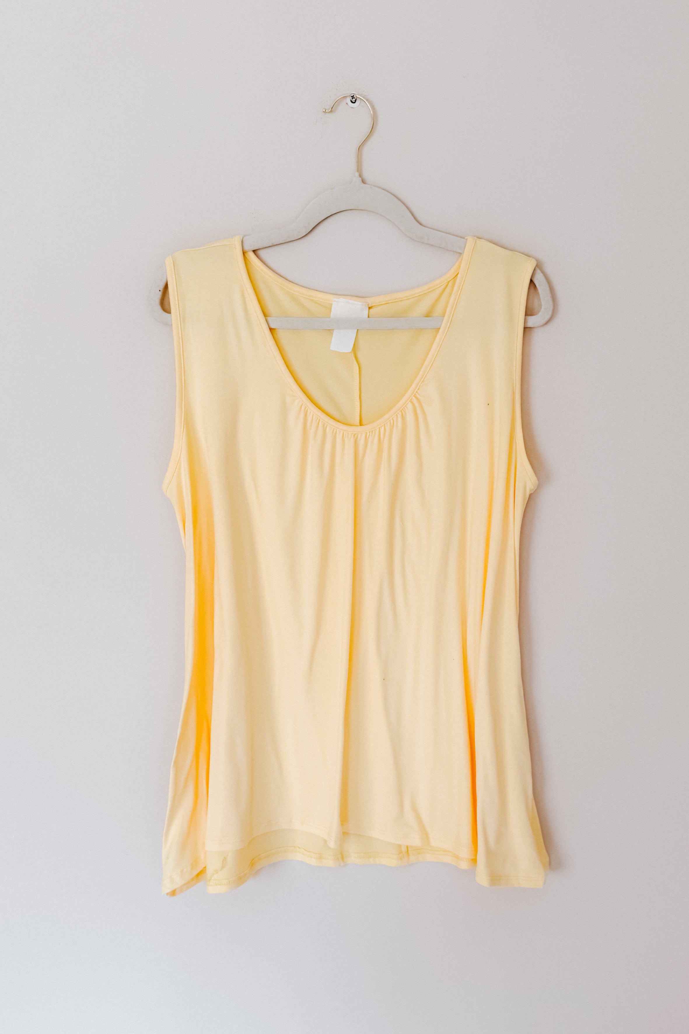 Soft yellow Banana Bliss tank top with scoop neckline hanging on clear hanger against plain wall