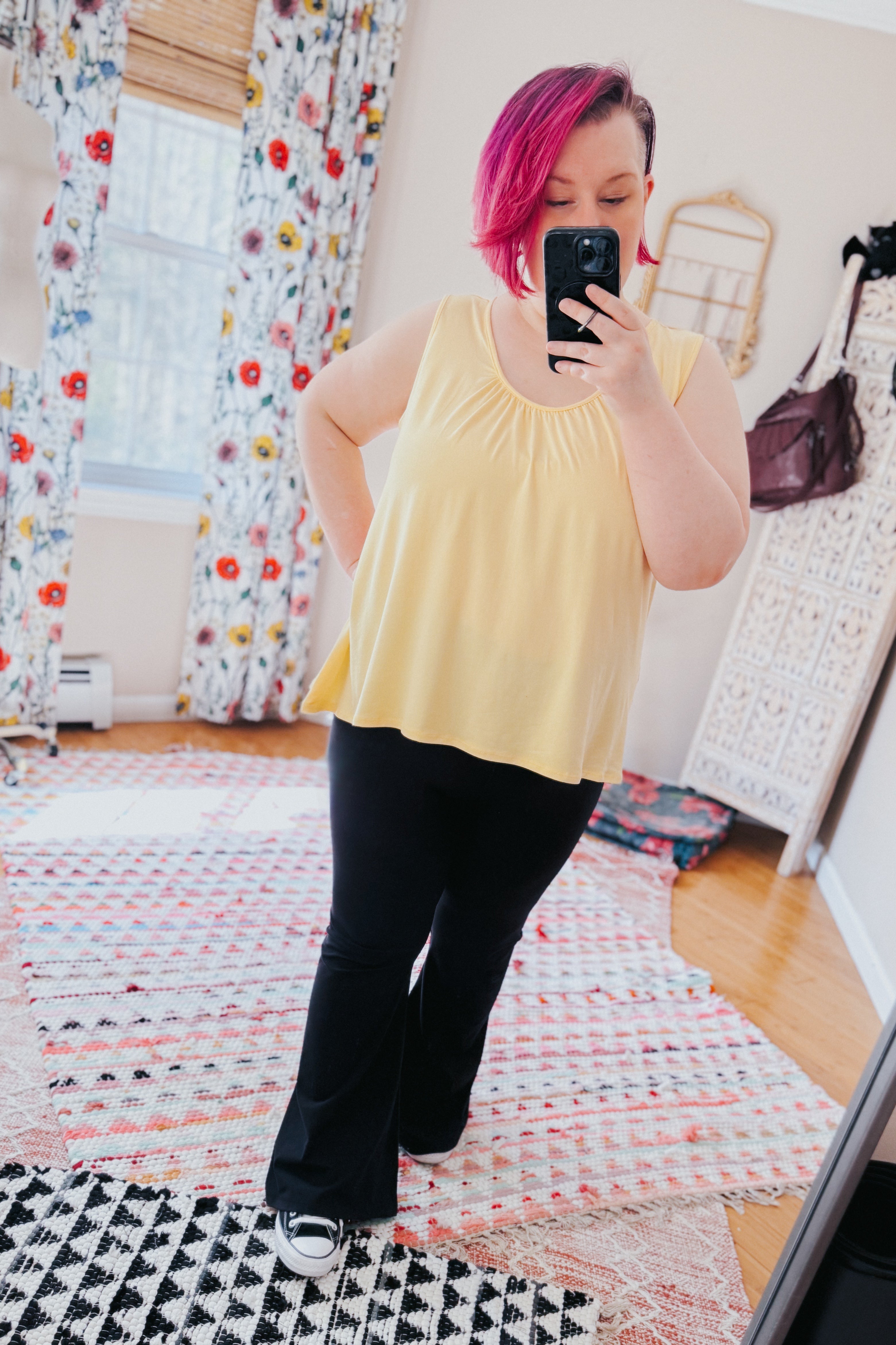 Person with pink hair taking indoor mirror selfie wearing flowy yellow Banana Bliss tank top and black pants