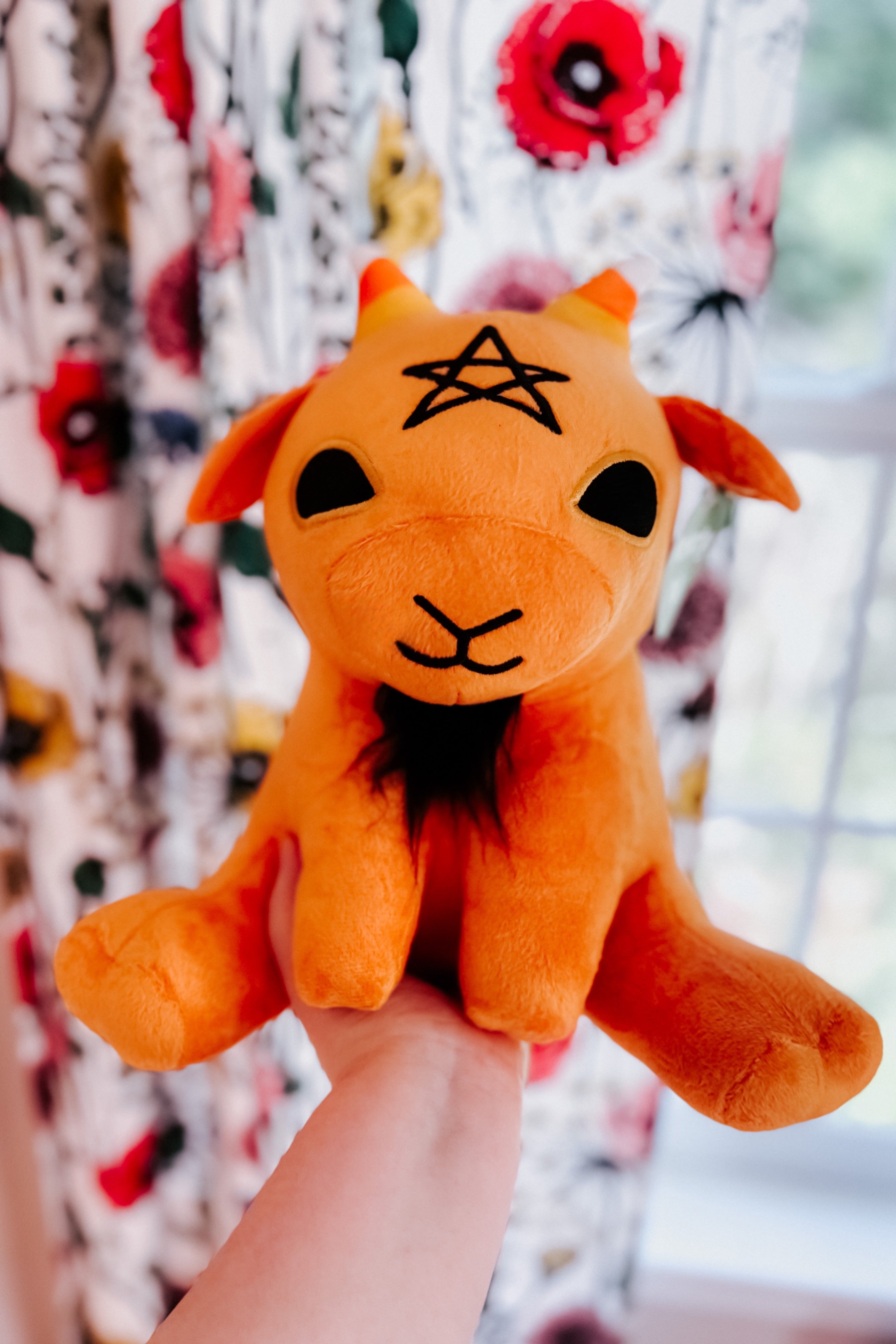 Hand holding front-facing pumpkin spice witchy baby goat plush with black star embroidery on forehead
