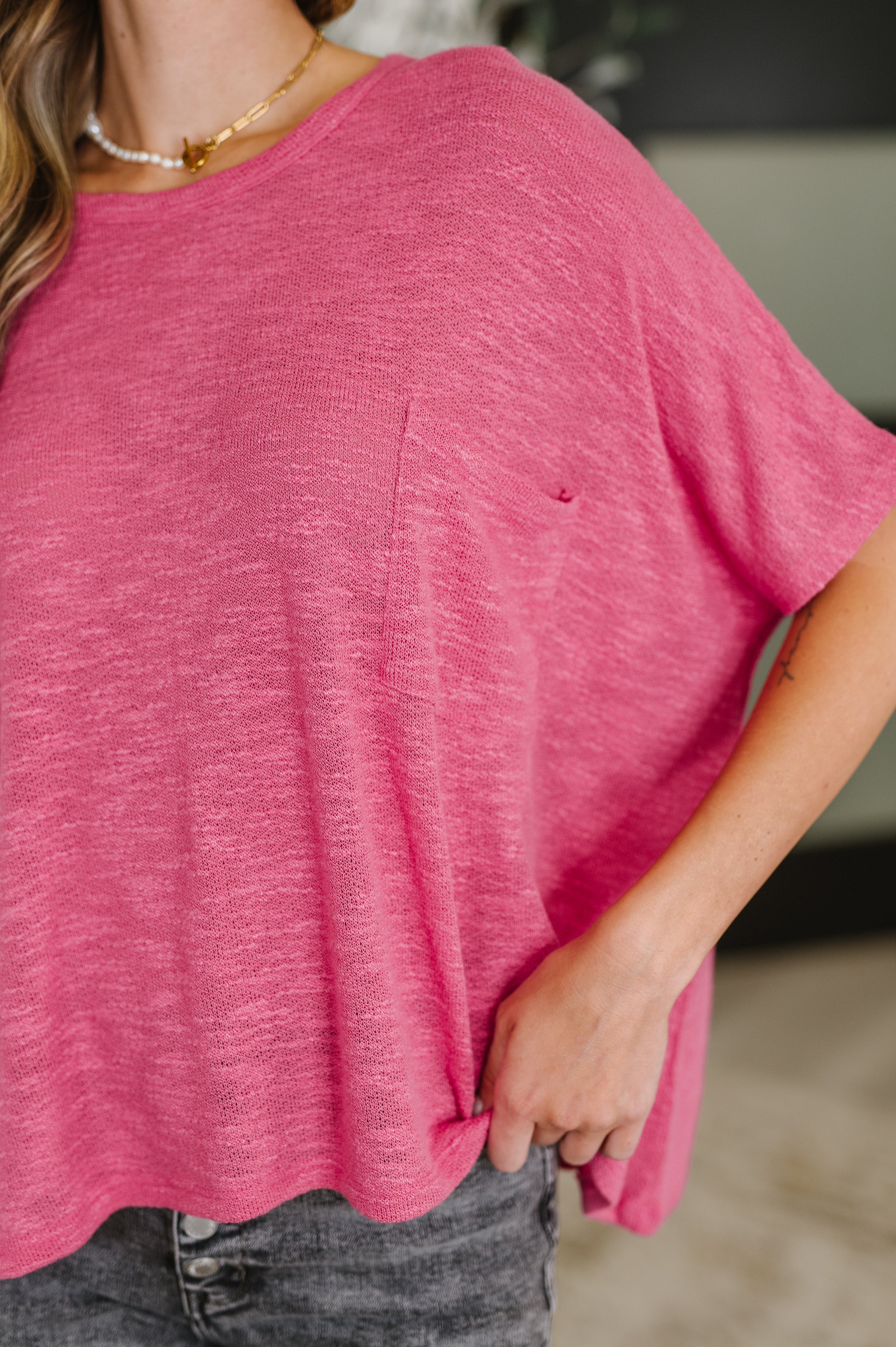 Close-up of hot pink flowing dolman sleeve top with subtle pocket and soft textured fabric worn with faded black jeans