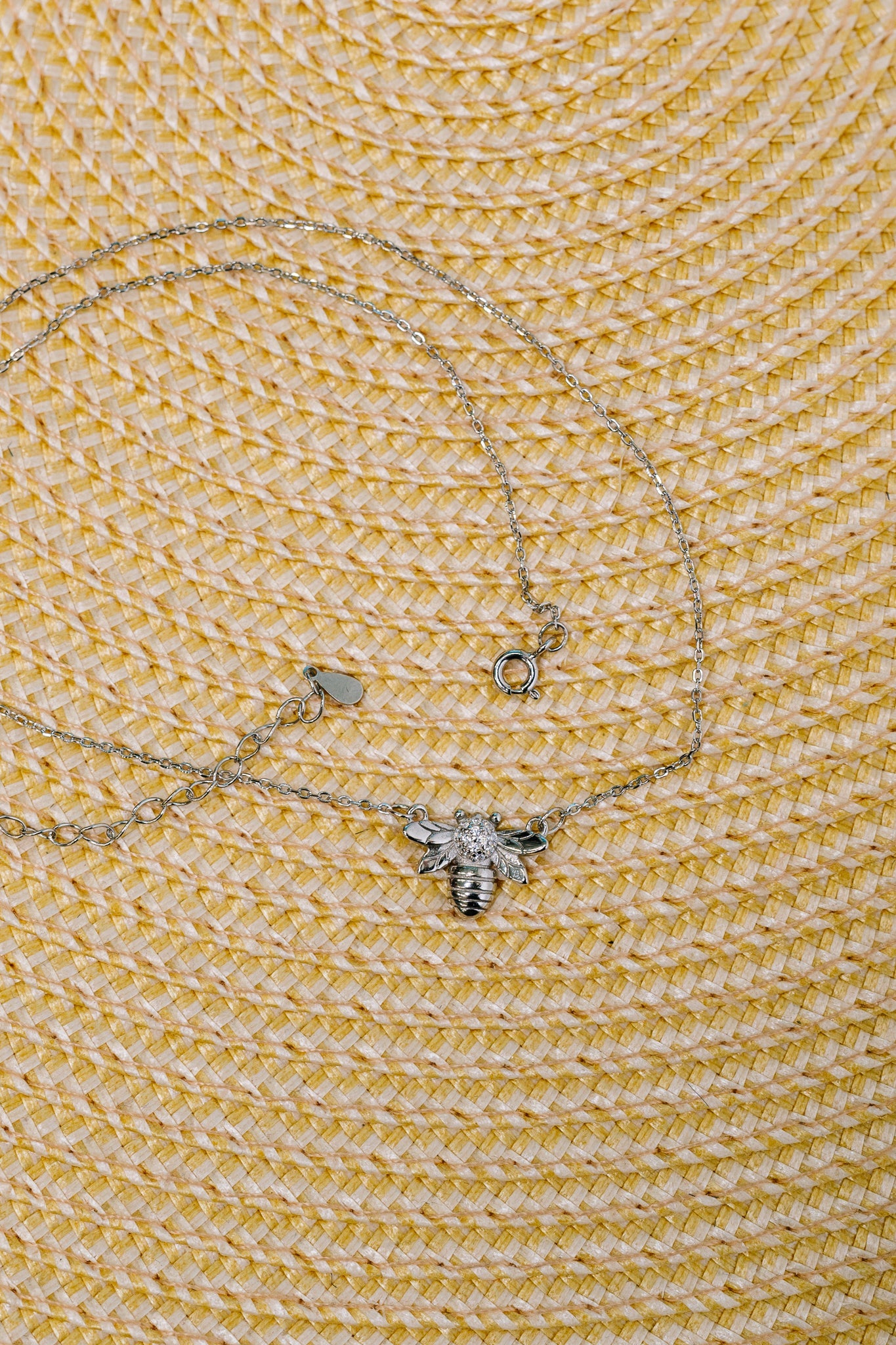Delicate silver necklace featuring a bee pendant with sparkling stones on a textured yellow background