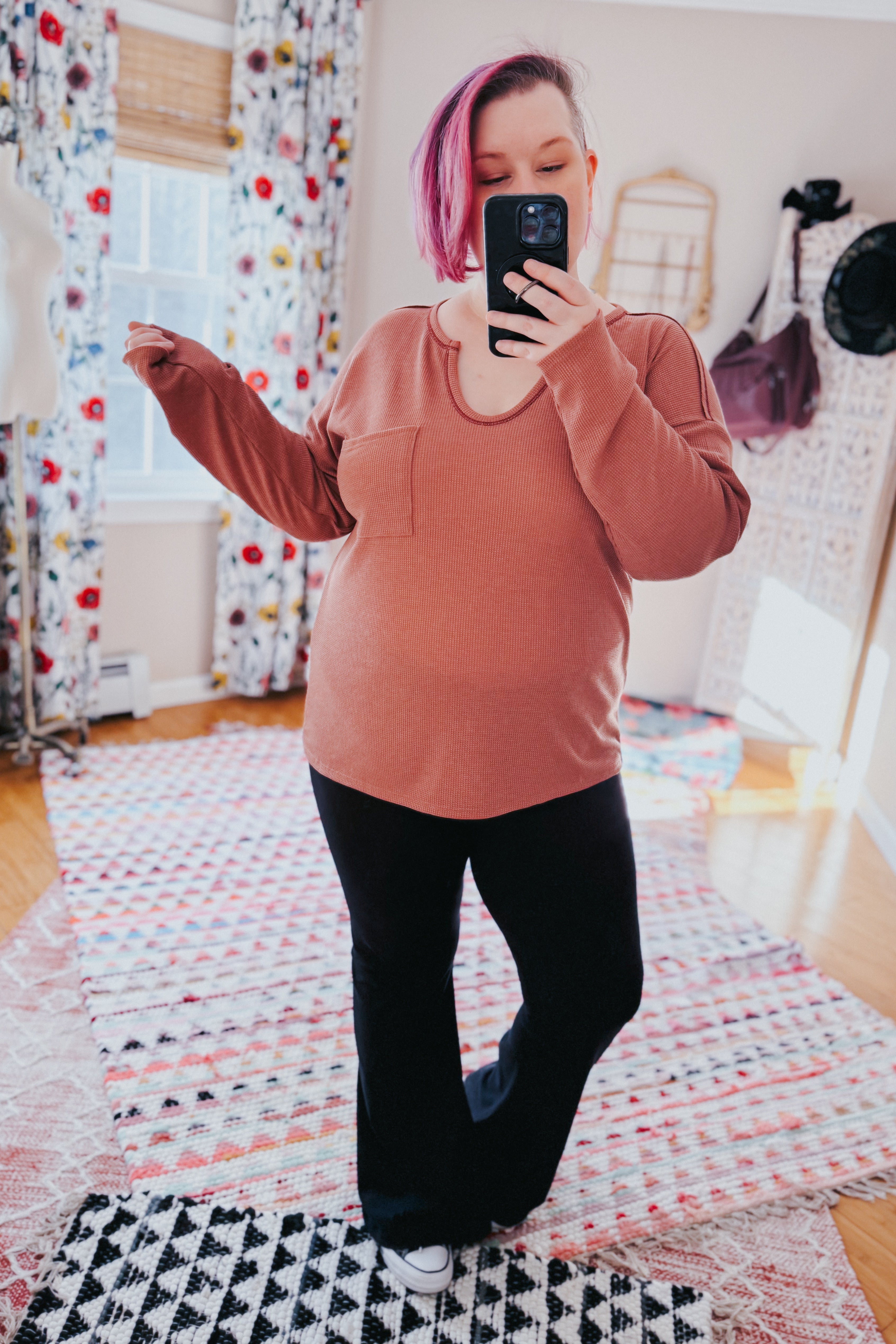 Person with pink hair taking mirror selfie wearing rust-colored Behind The Scenes waffle knit top with pocket and black pants in patterned room