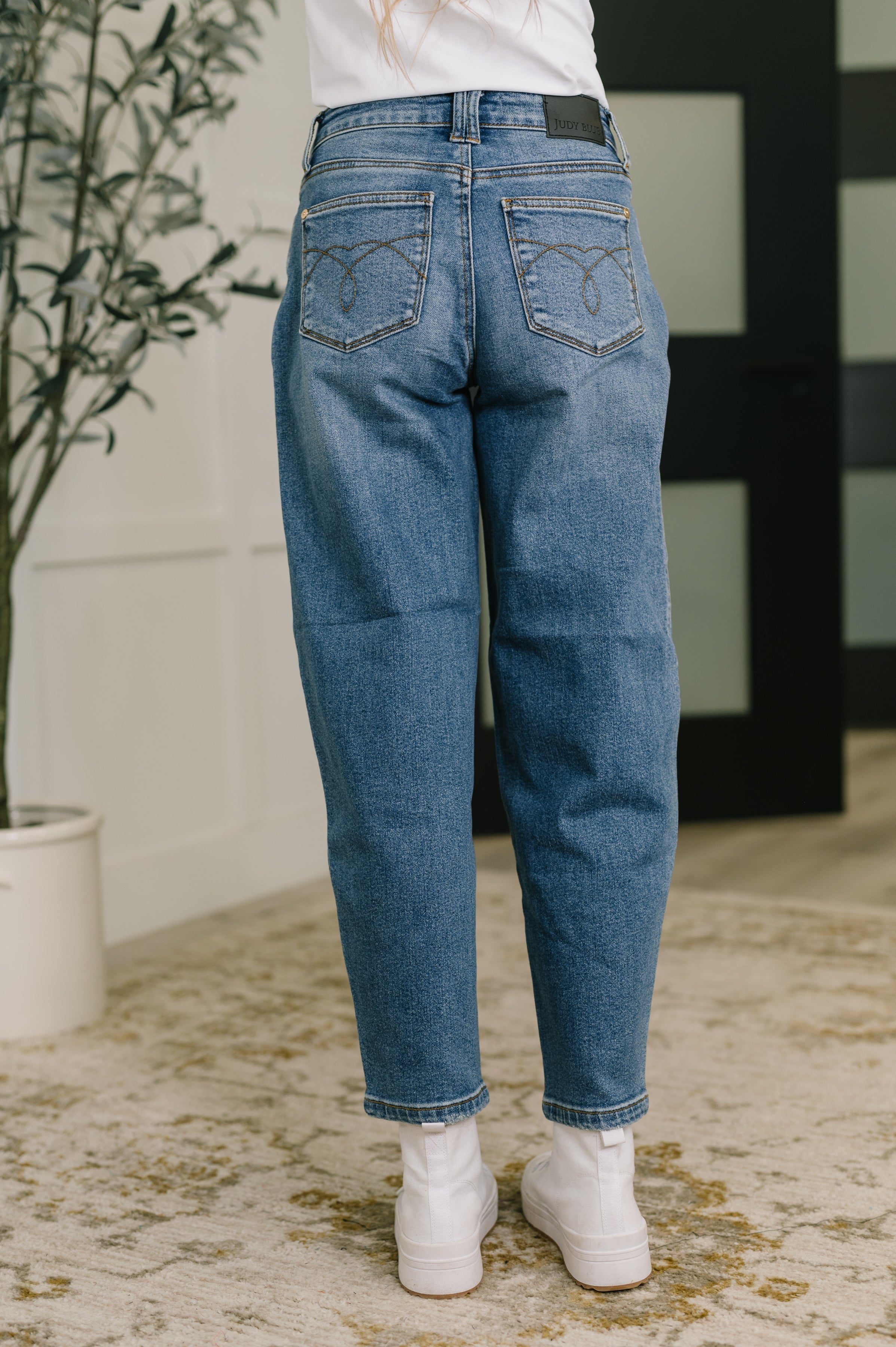 Back view of Bella High Waist jeans with soft barrel stitch pockets worn with white sneakers indoors