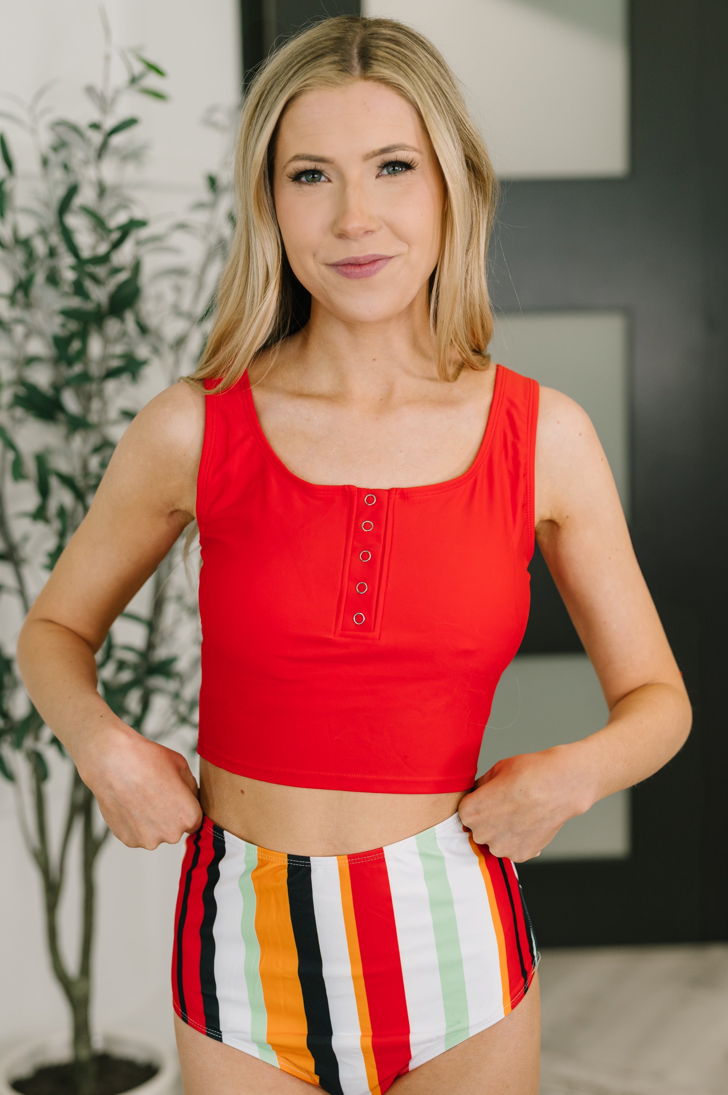 Woman wearing a vibrant red sleeveless crop top with front snap buttons paired with high-waisted striped bottoms