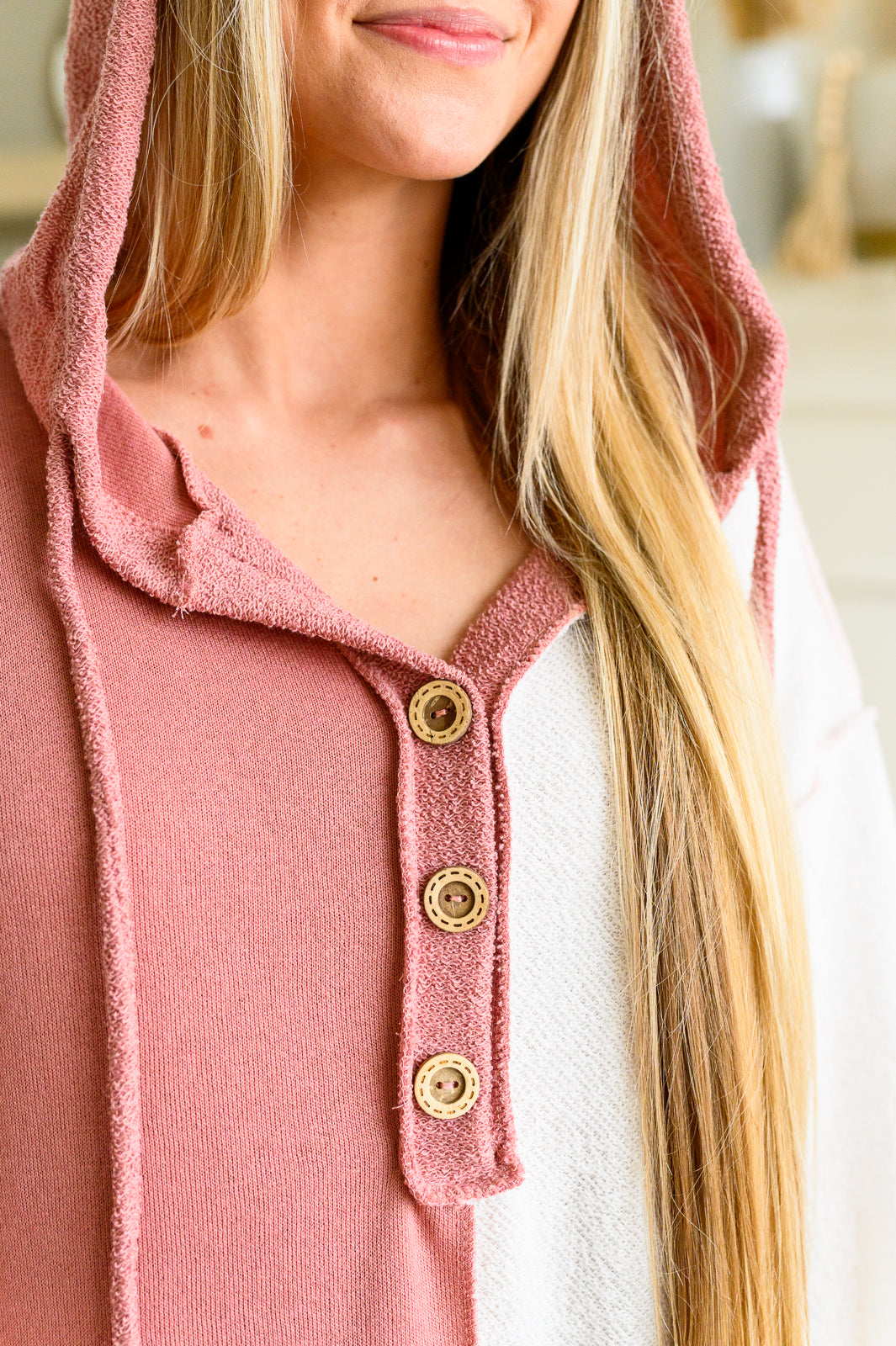 Close-up of woman wearing pink and white color block hoodie with wooden buttons and long blonde hair