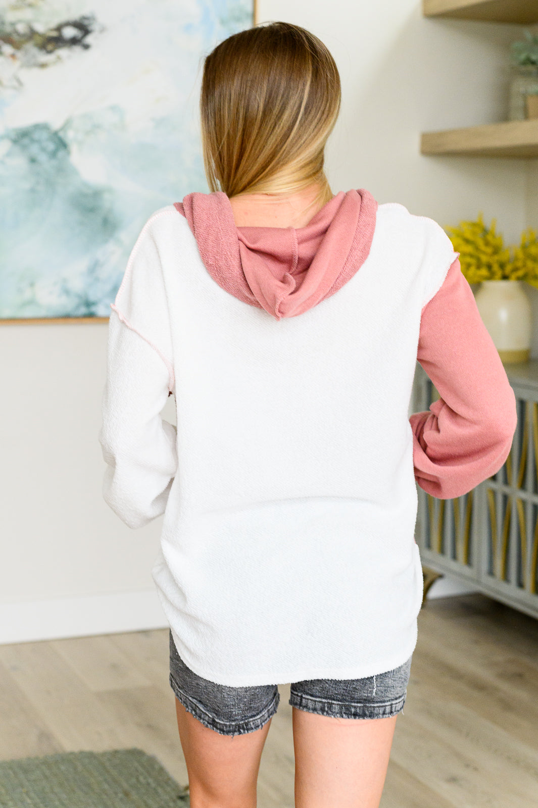 Woman wearing white and dusty rose color block hoodie standing indoors with back facing camera