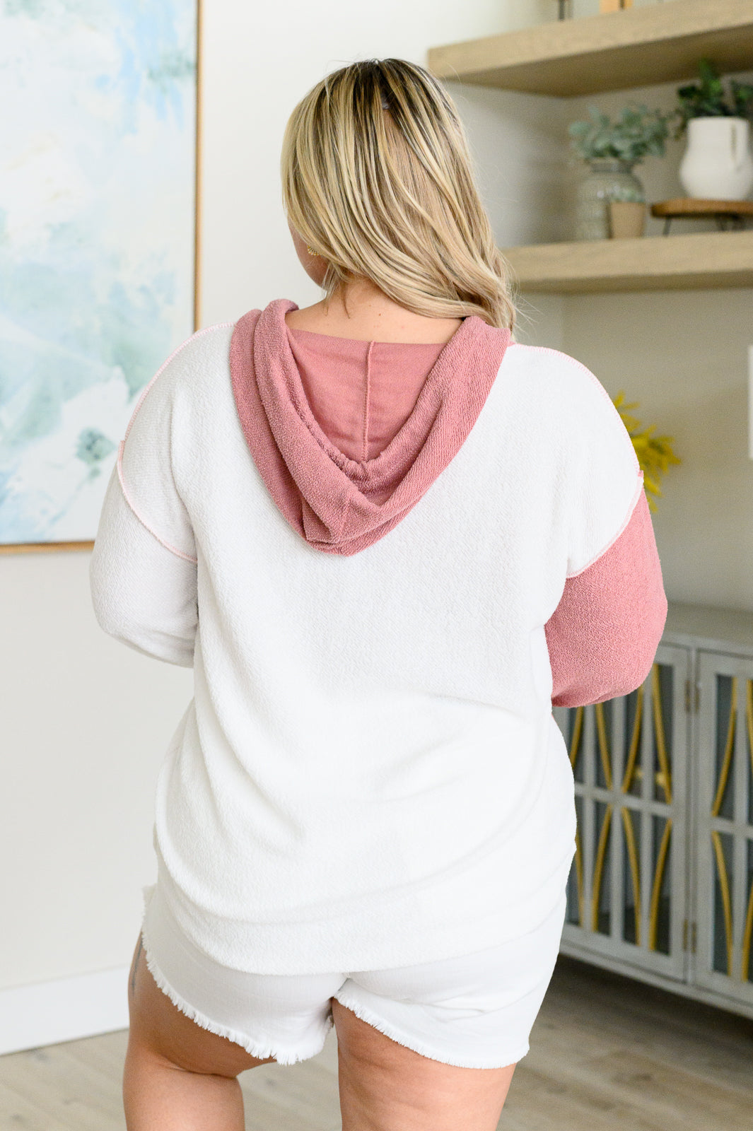 Plus size woman wearing white and pink color block hoodie with hood standing indoors near shelving unit