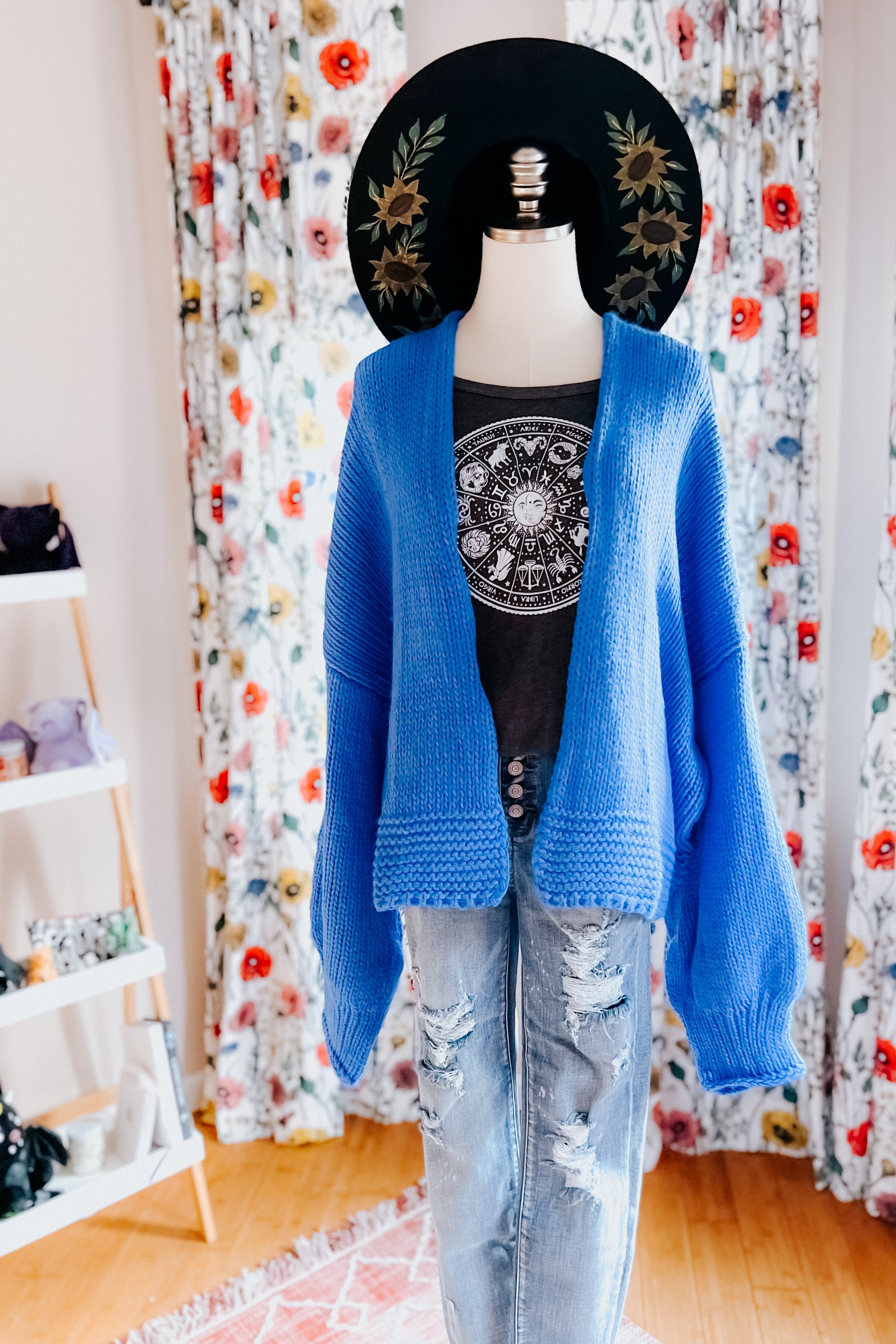 Mannequin dressed in bright blue oversized cardigan paired with black graphic tee and distressed light blue jeans indoors