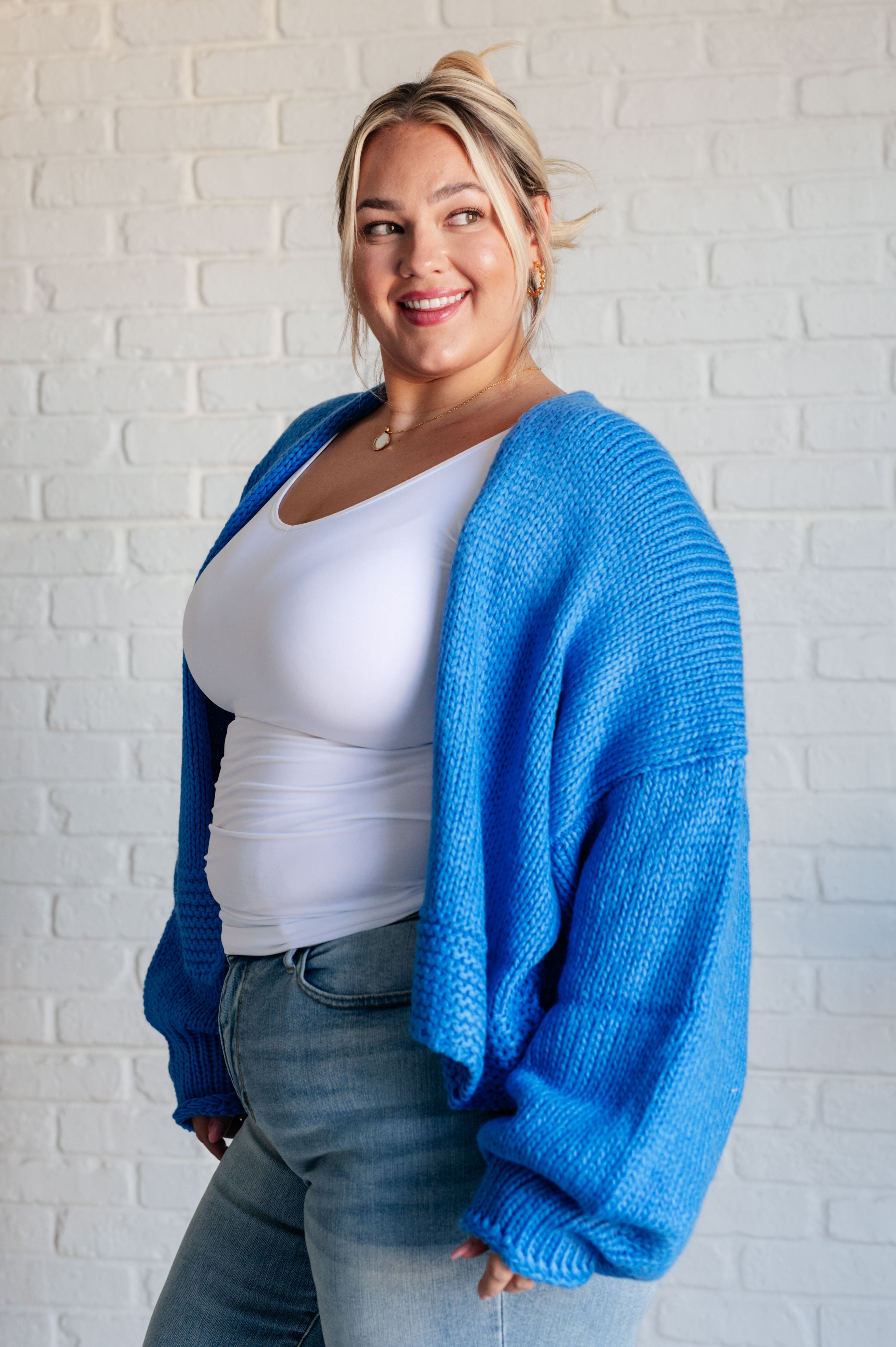 Plus size woman smiling wearing bright blue oversized knit cardigan over white tank top and light wash jeans