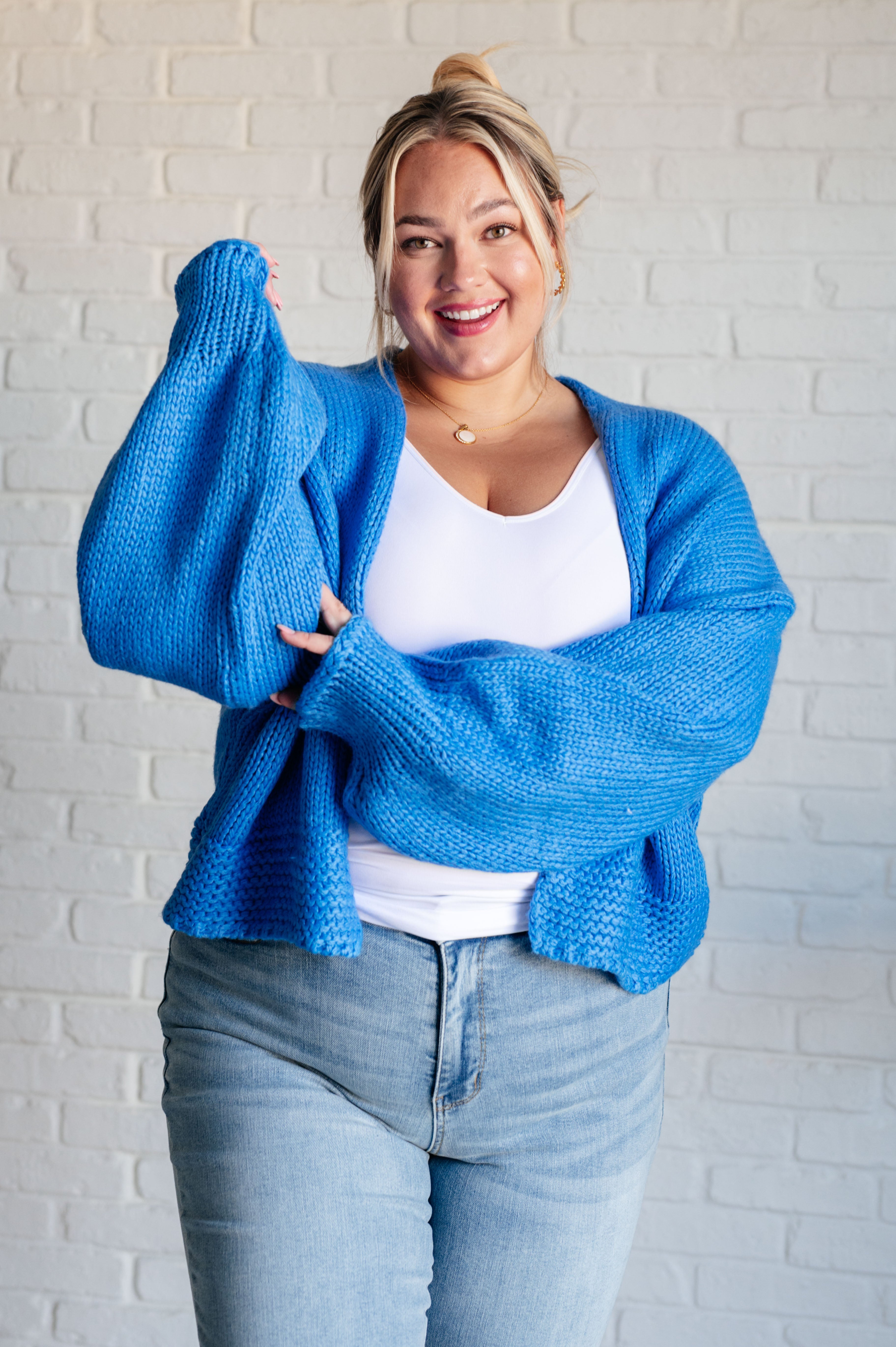 Smiling plus size woman wearing bright blue chunky knit cardigan over white tank and light wash jeans indoors