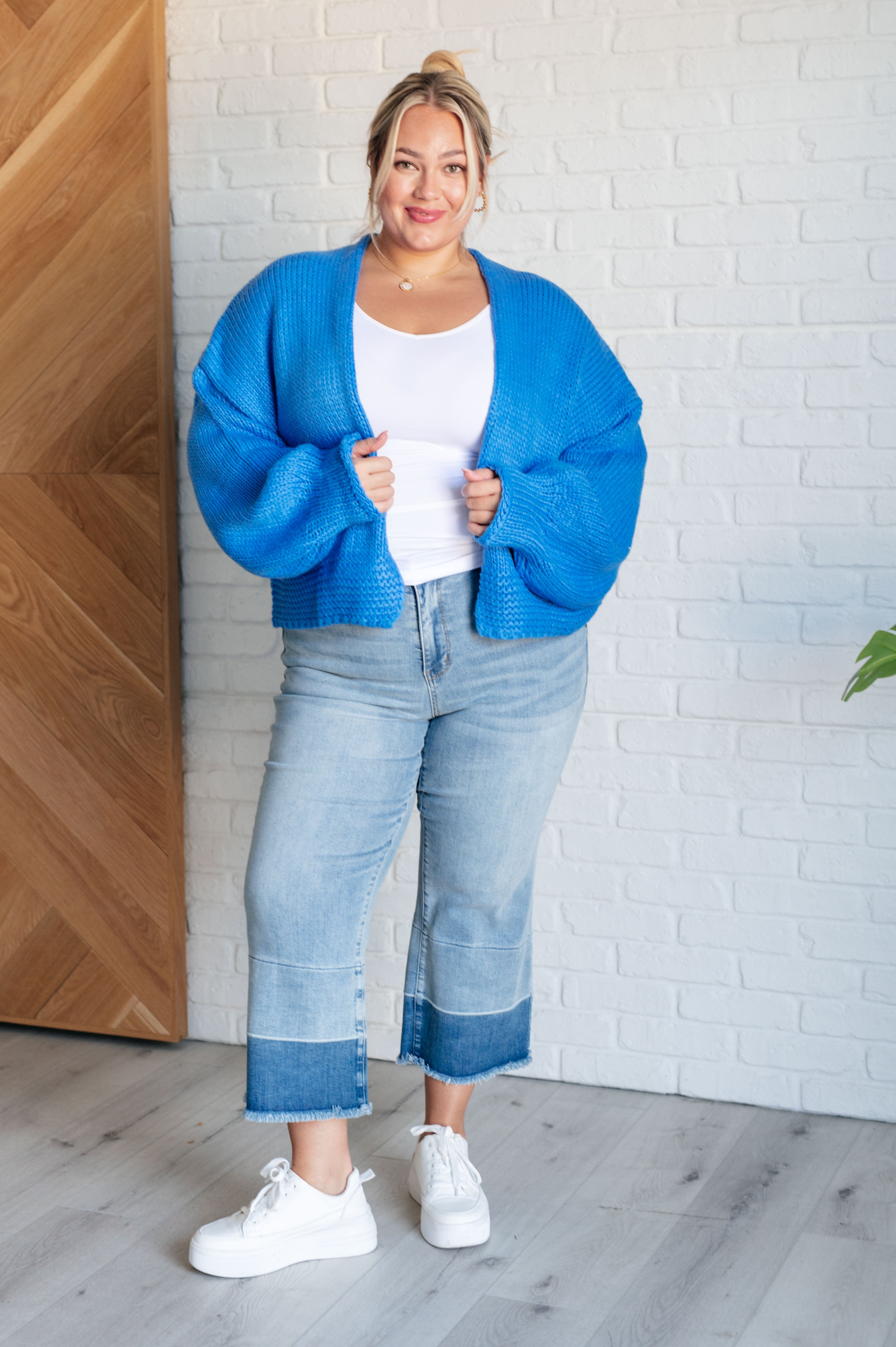 Plus size woman wearing bright blue chunky knit cardigan over white tank top and cropped two-tone wide leg jeans