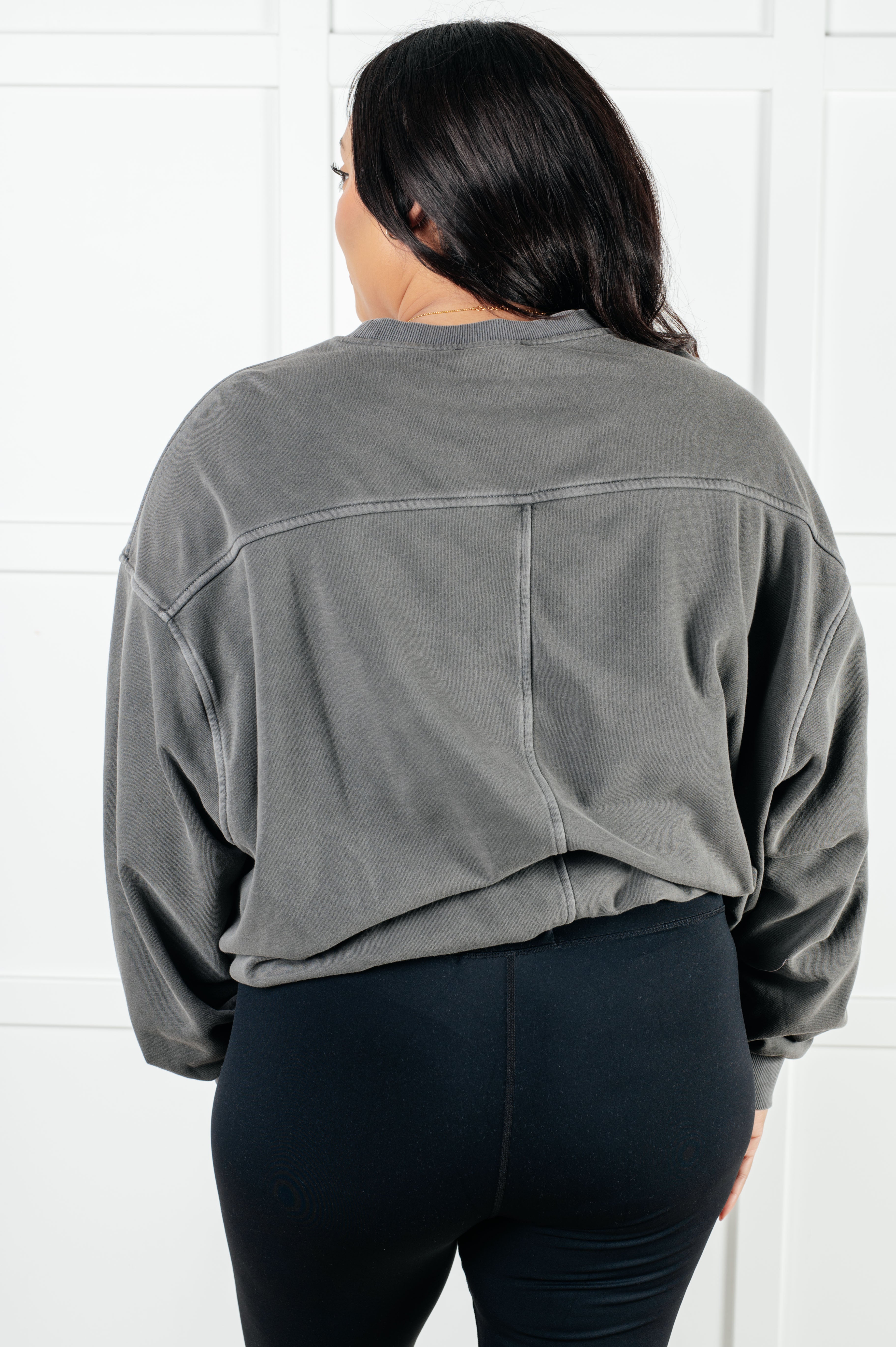 Rear view of person wearing loose ash black pullover with dropped shoulders and black fitted pants against white background