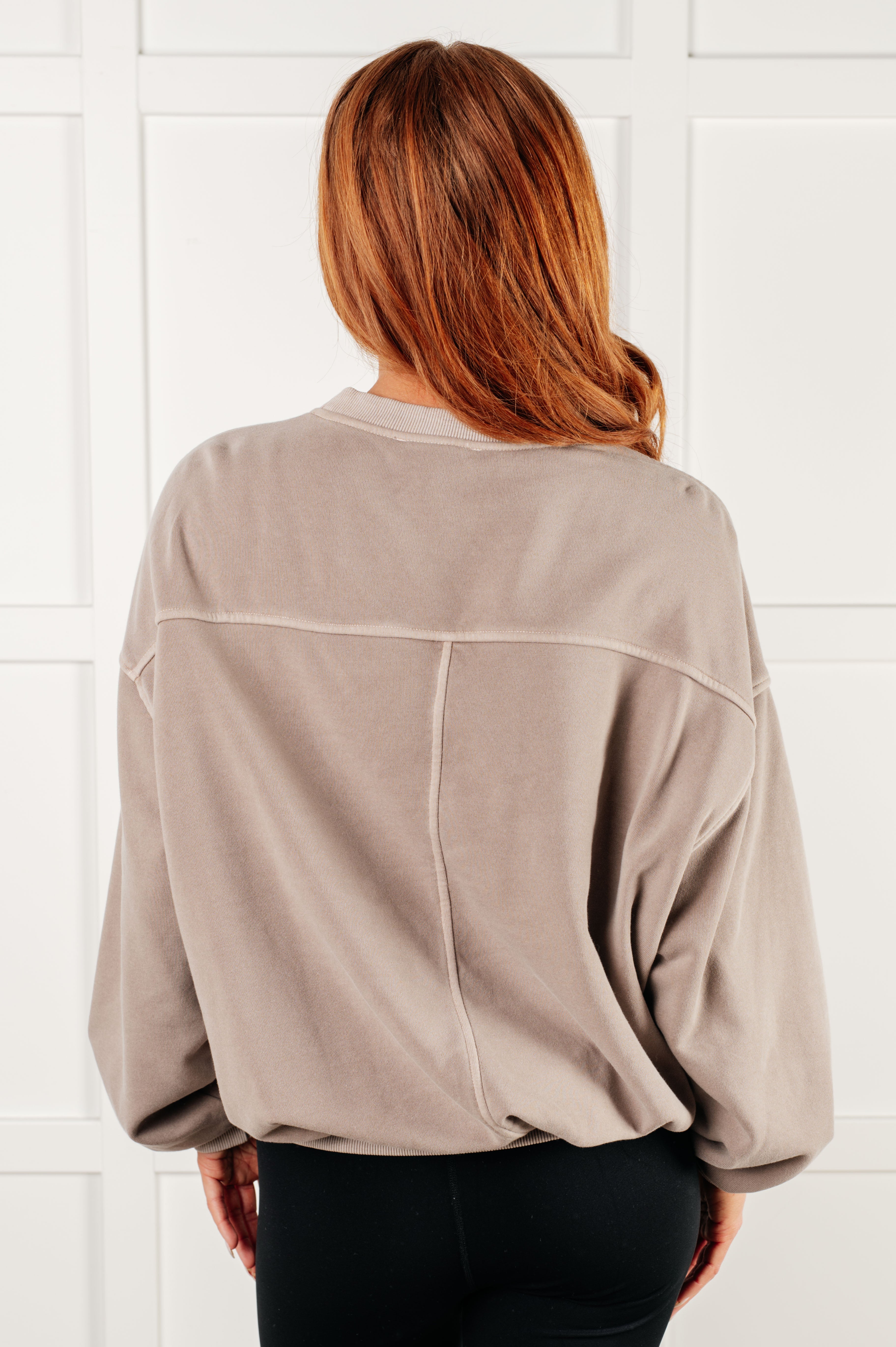 Woman with shoulder-length auburn hair wearing loose ash mocha pullover with dropped shoulders against white paneled wall