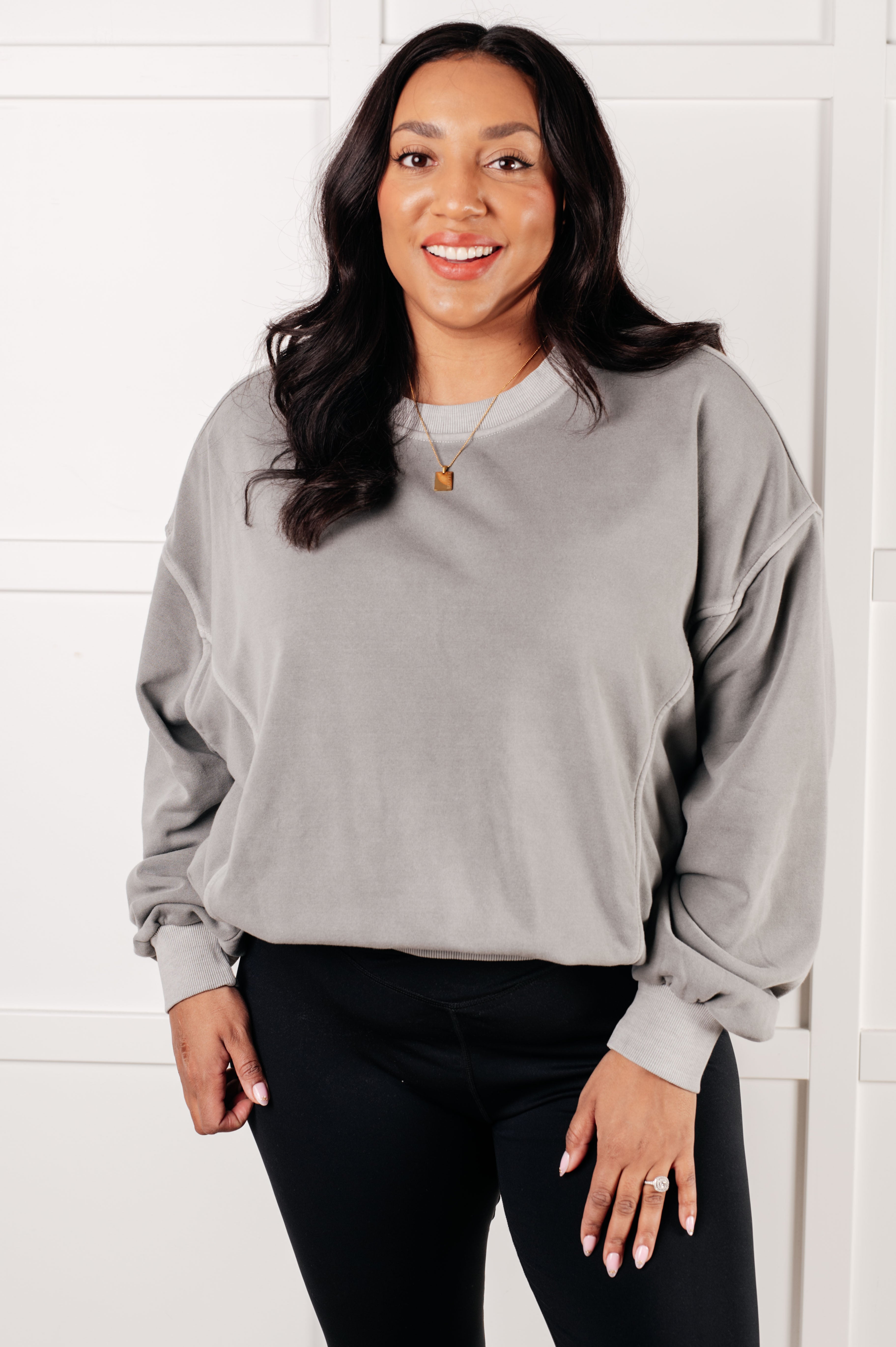 Smiling woman wearing loose fit gray Beyond the Basics Pullover with black leggings and gold pendant necklace indoors
