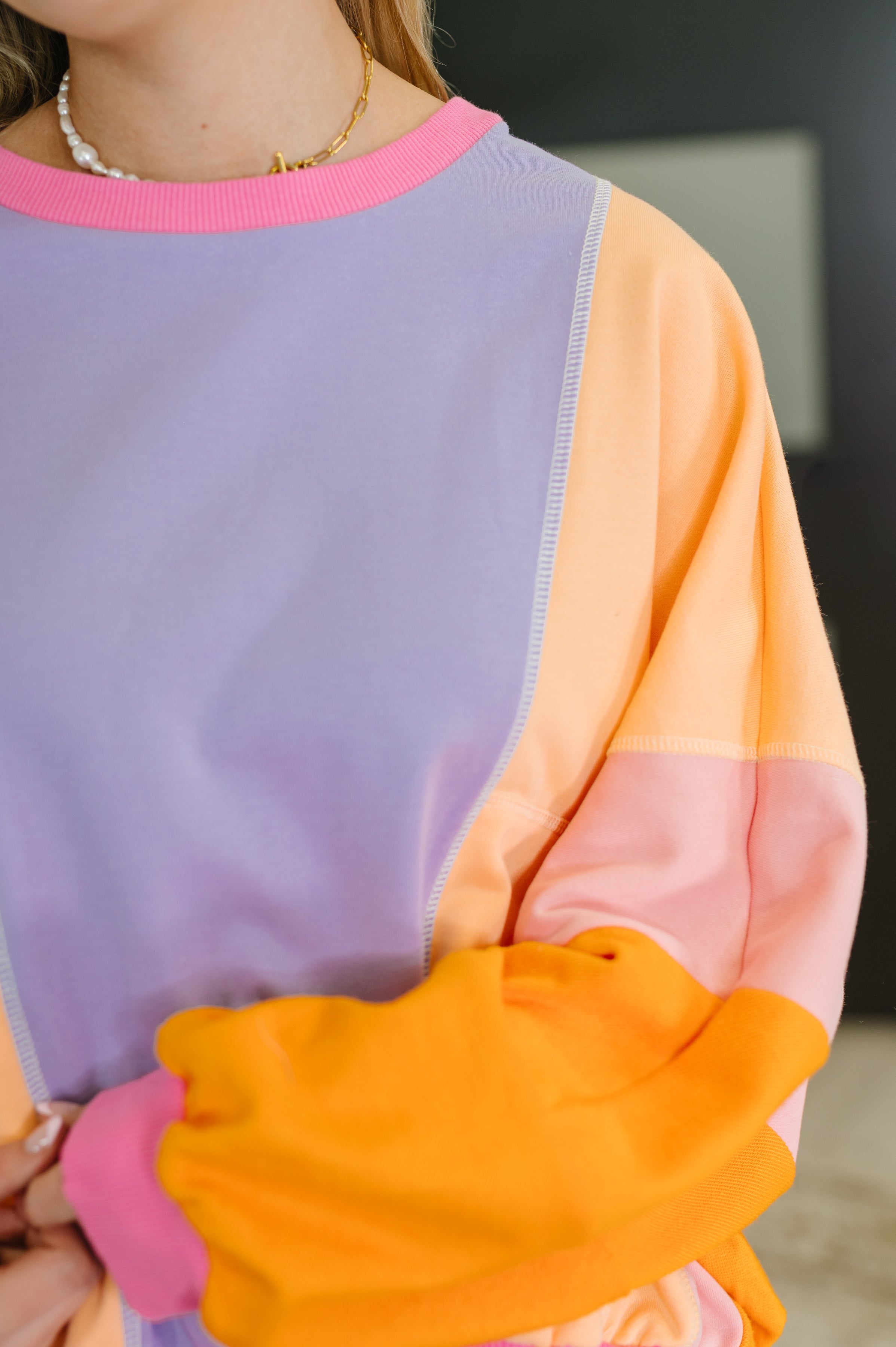 Close up of woman wearing a purple and yellow color block pullover with pink and orange dolman sleeves